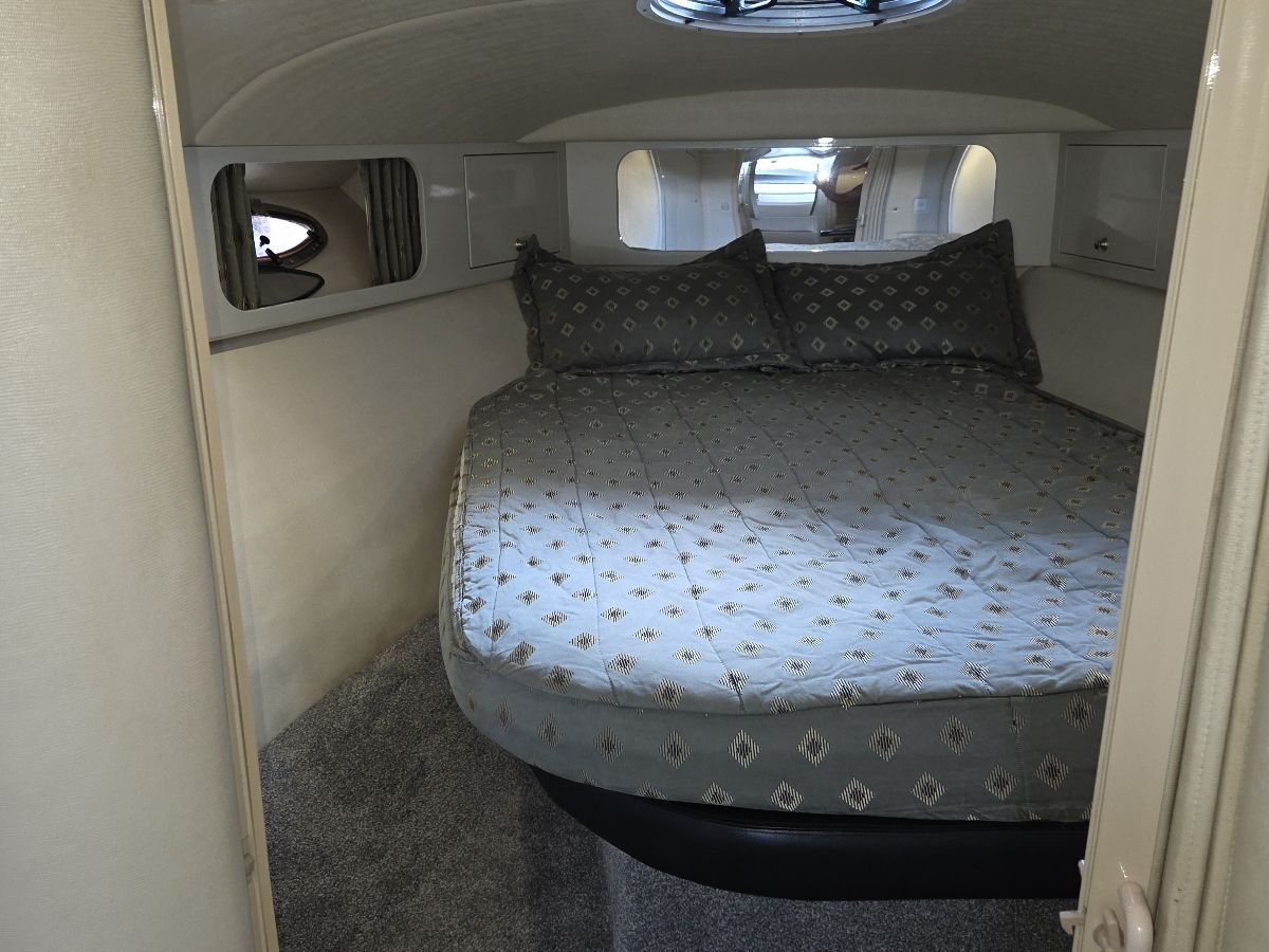 The image shows a cozy cabin with a large, cushioned bed and round windows.