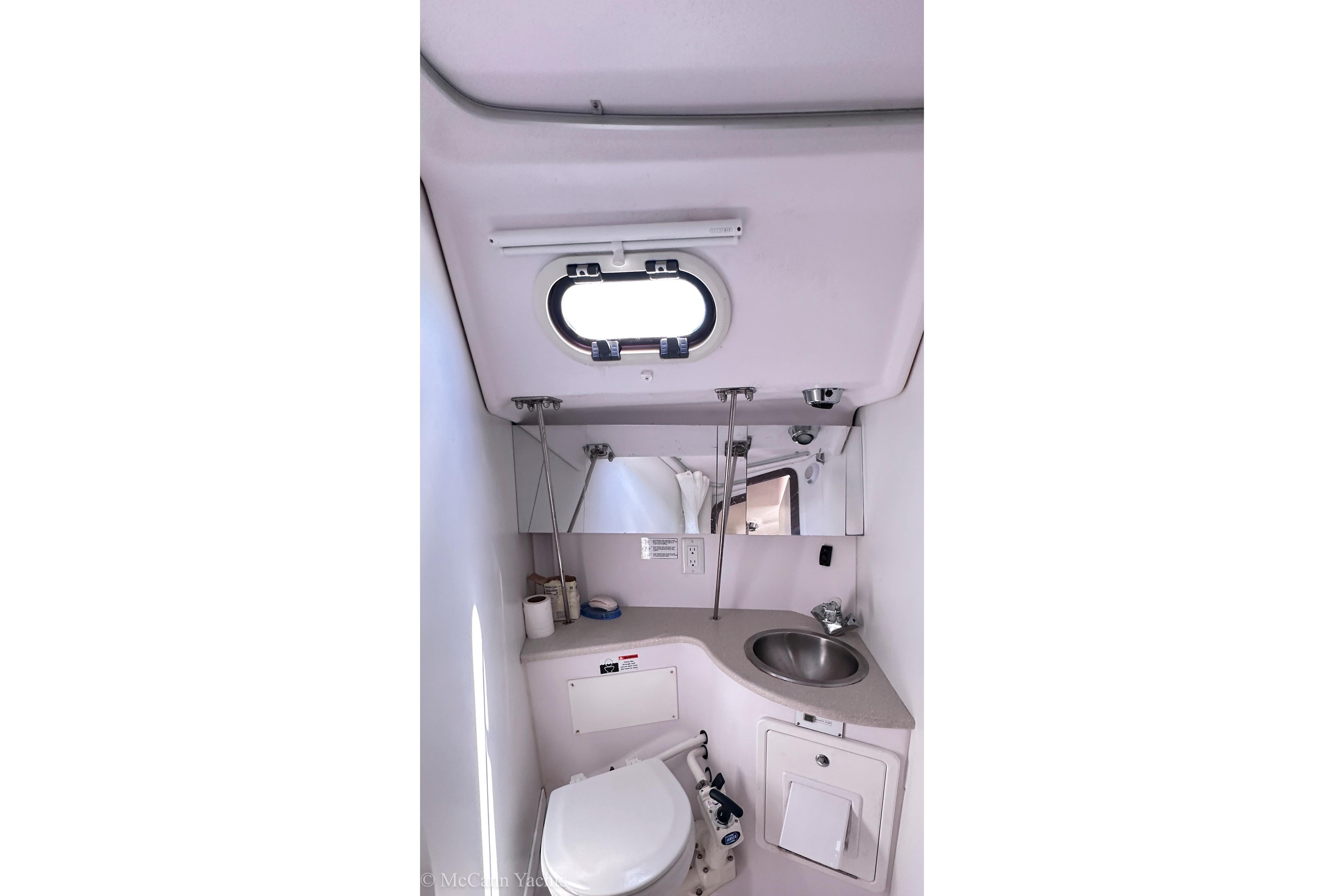 Compact bathroom in a 2015 Catalina 315 yacht with sink, toilet, and porthole window.