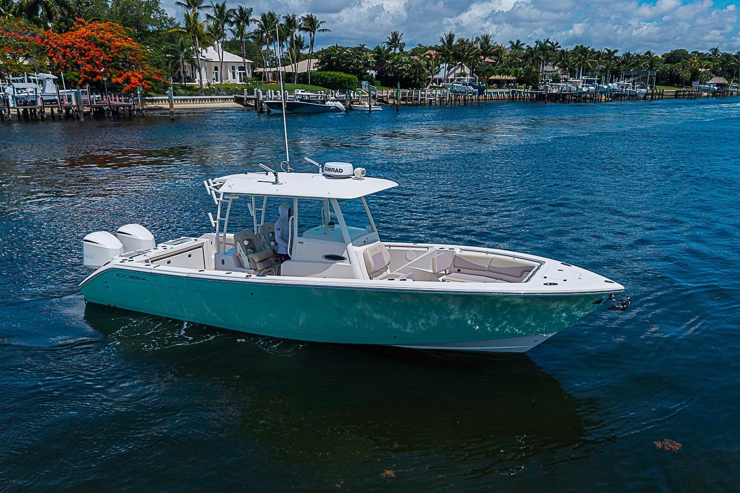 2019 Cobia 320 Center Console boat on calm water, surrounded by lush greenery.