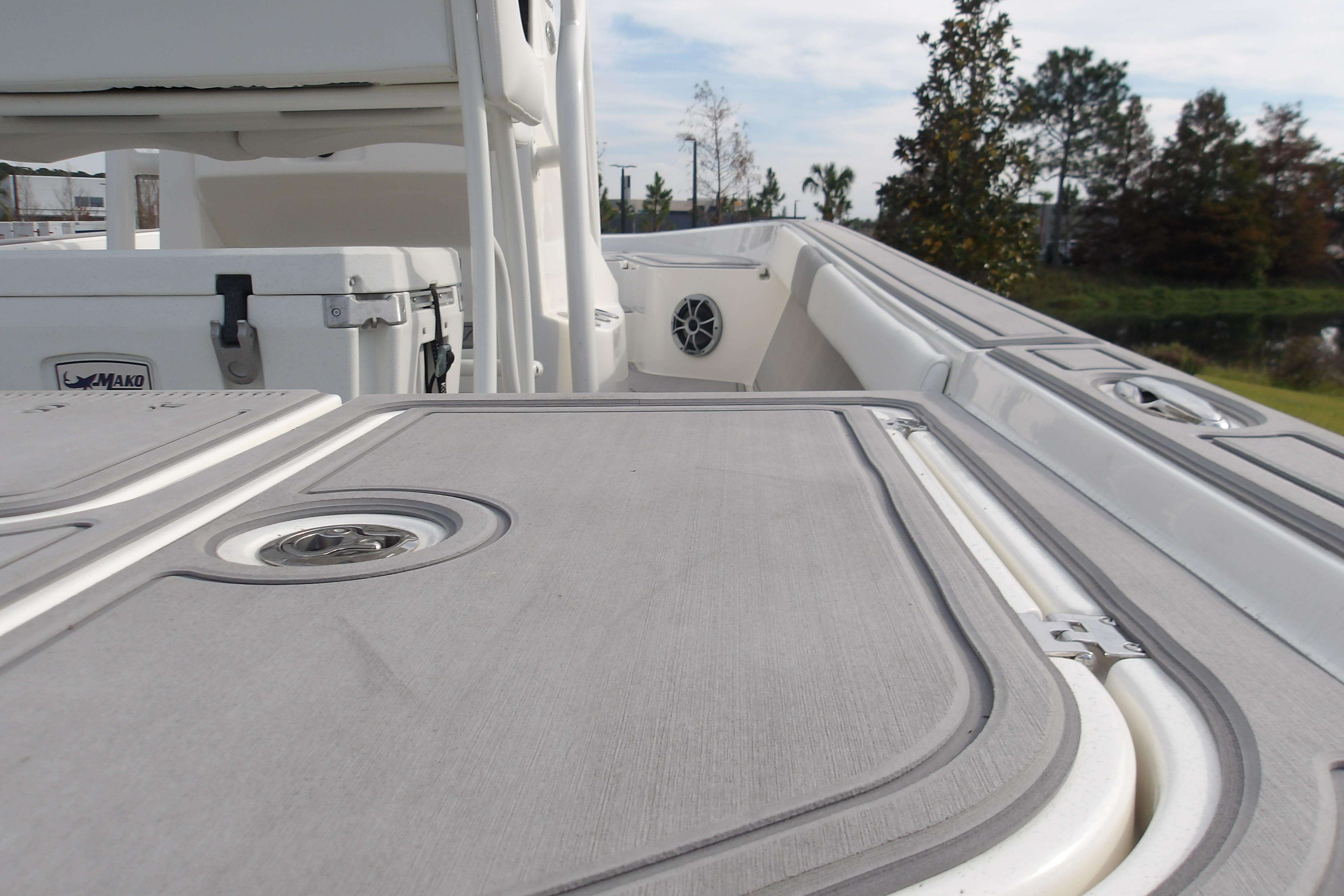 2026 Mako 24 APEX boat deck with storage compartments and cooler, surrounded by greenery.