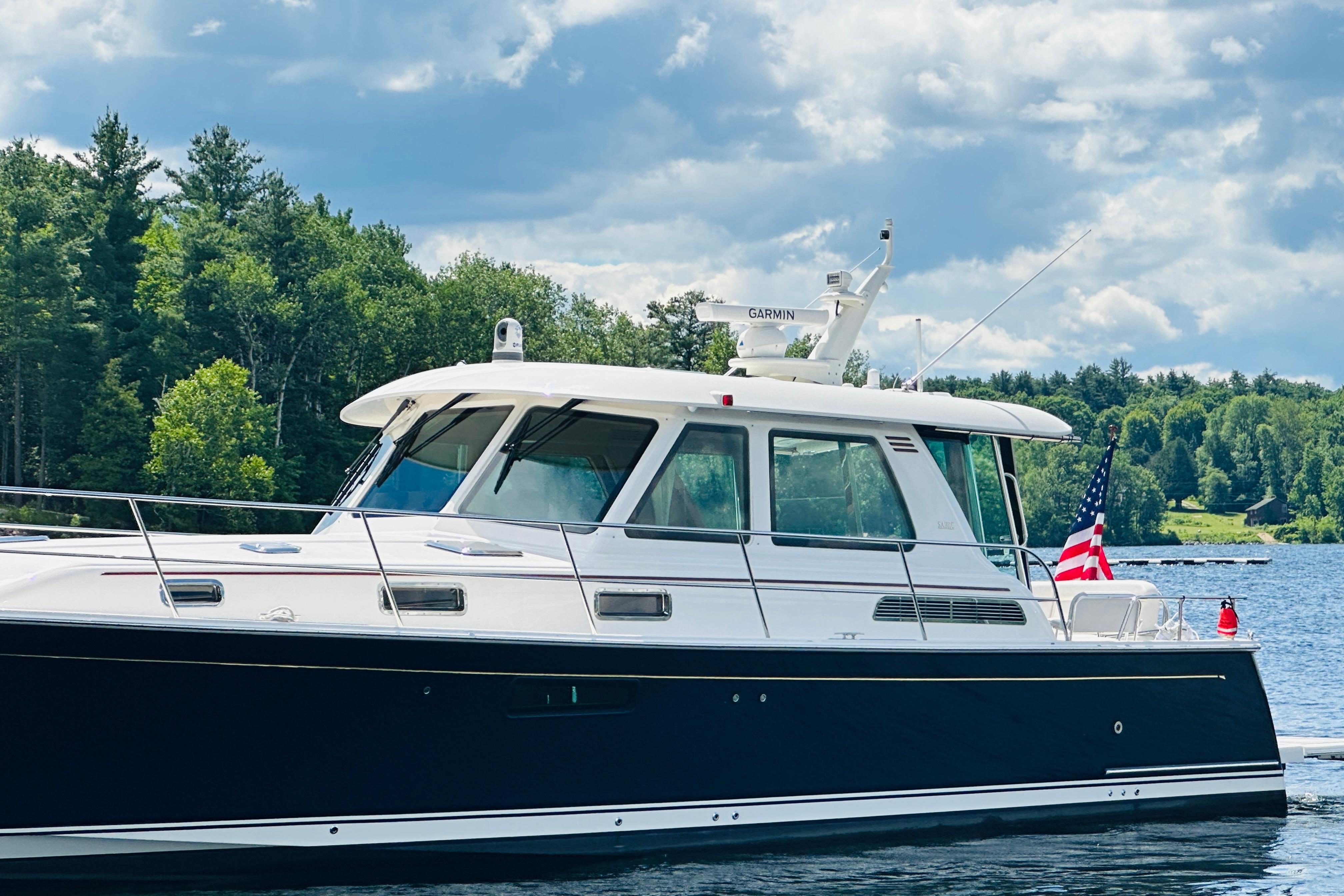 2025 Sabre 48 Salon Express yacht cruising on a serene lake with lush green trees.