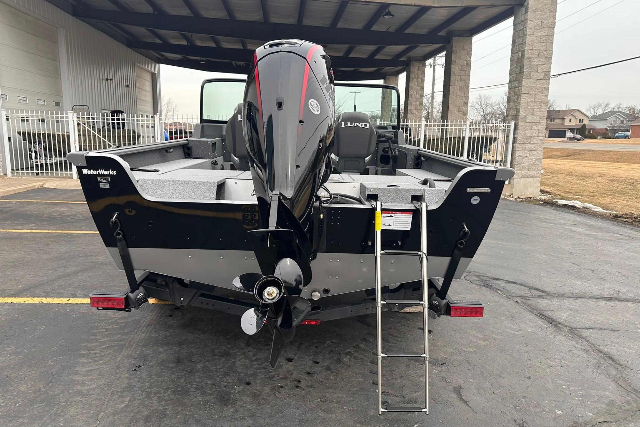 2026 Lund 1775 Impact XS Sport boat with outboard motor and ladder, parked outdoors.