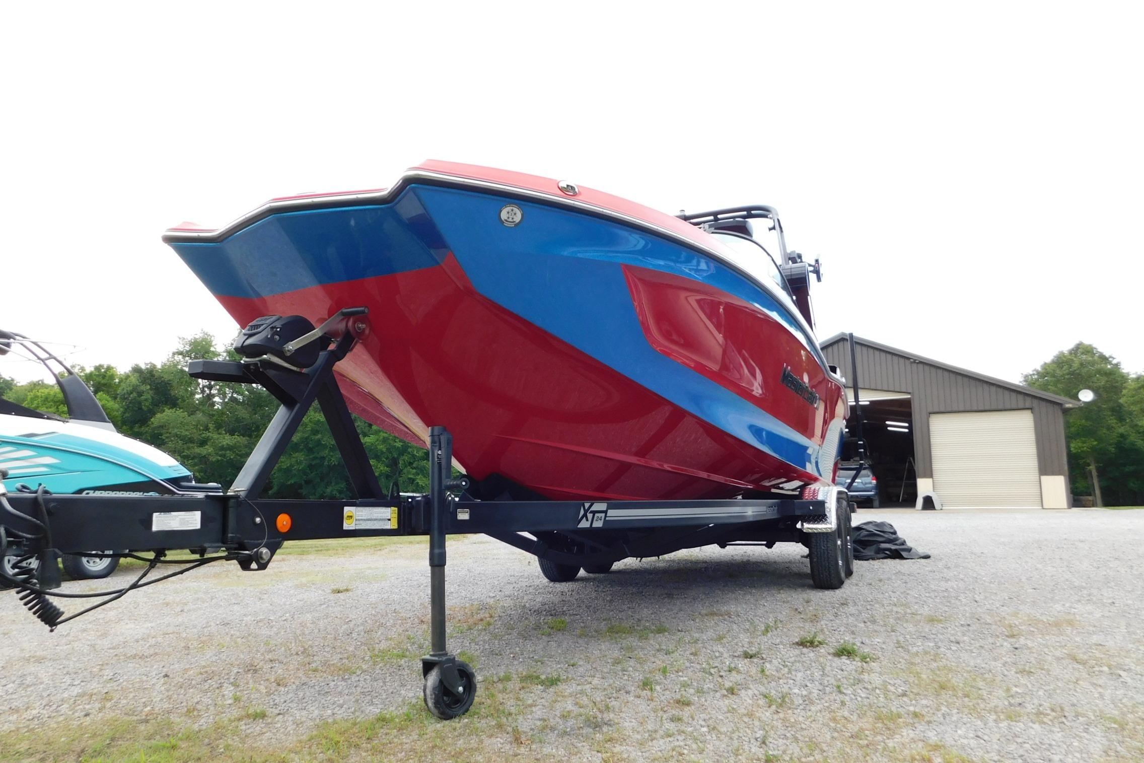2022 MasterCraft NXT24 boat on trailer, vibrant red and blue design, parked outdoors.