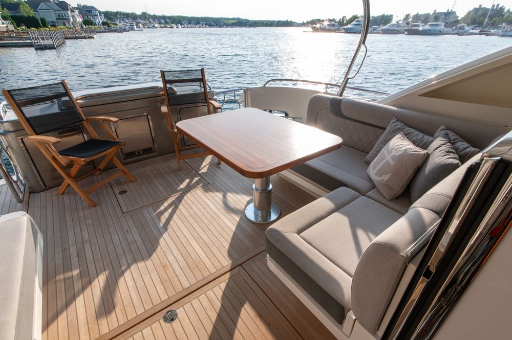 Luxurious 2022 Riviera 6000 Sport Yacht Platinum deck with seating and table, overlooking serene waters.