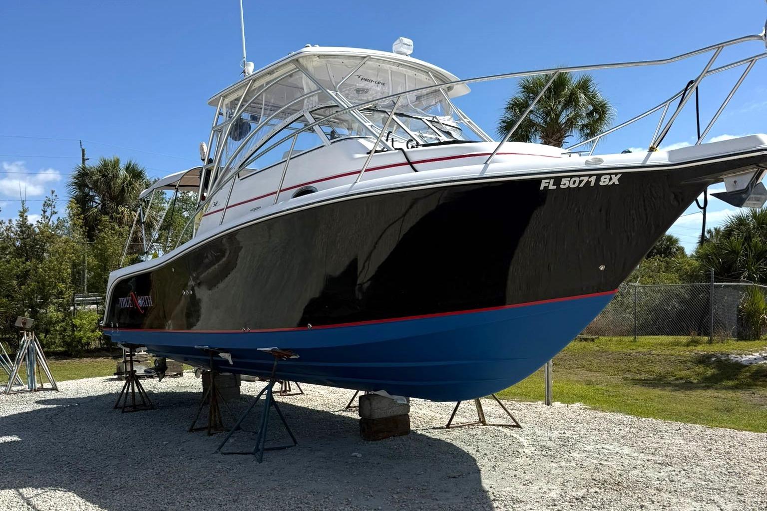 2006 Pro-Line 32 Express boat on stands, black and blue hull, sunny day.