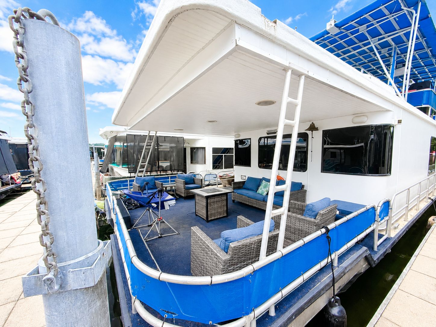 A spacious houseboat with blue accents docked. It features a cozy seating area.