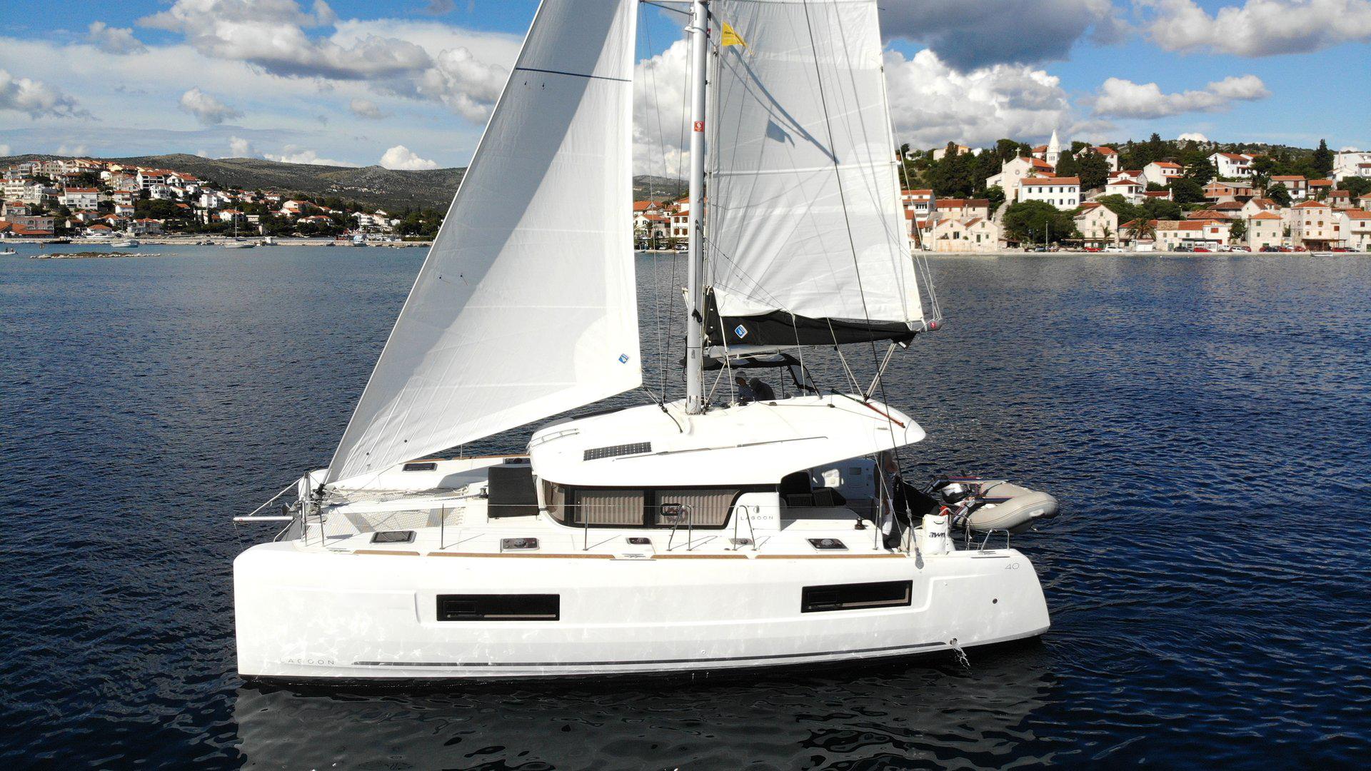 2019 Lagoon 40 catamaran sailing near coastal town under blue sky.