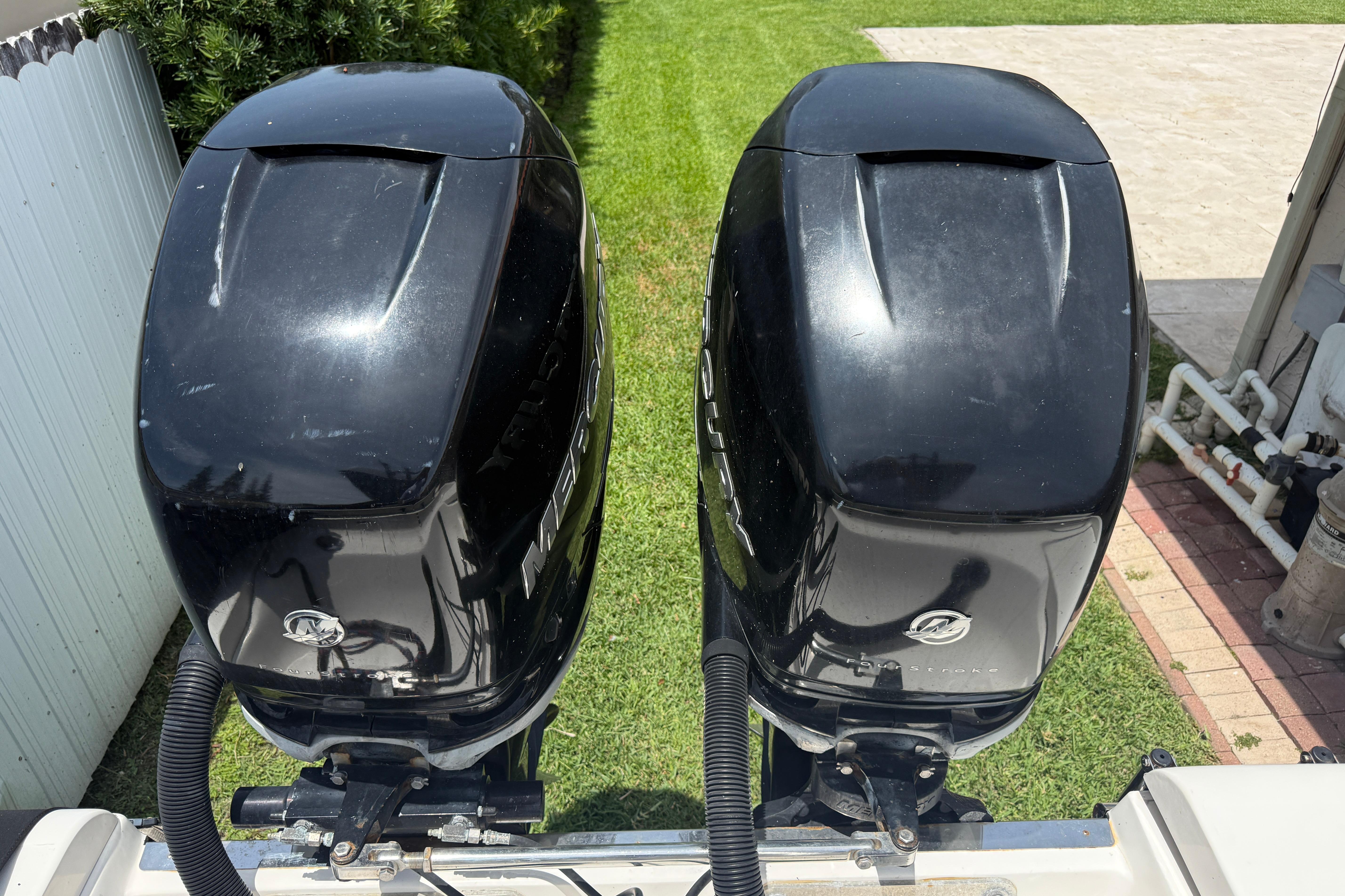Twin Mercury outboard engines on a 2015 Blackwood 27 boat, parked on grass.