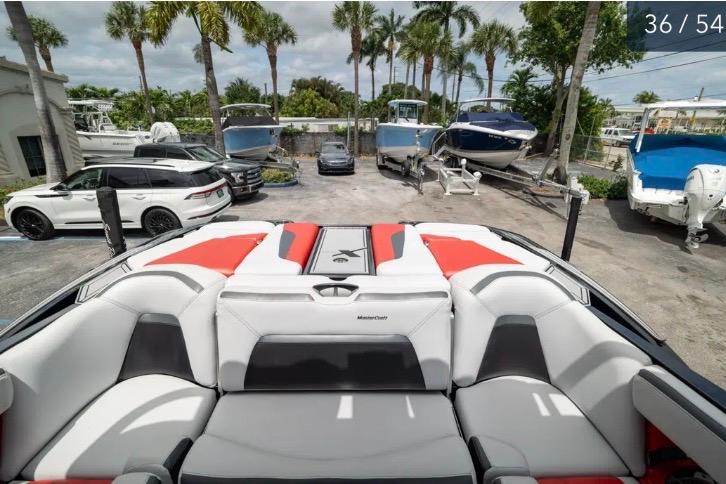 2019 MasterCraft XStar boat interior with red and gray seating, parked near palm trees and vehicles.