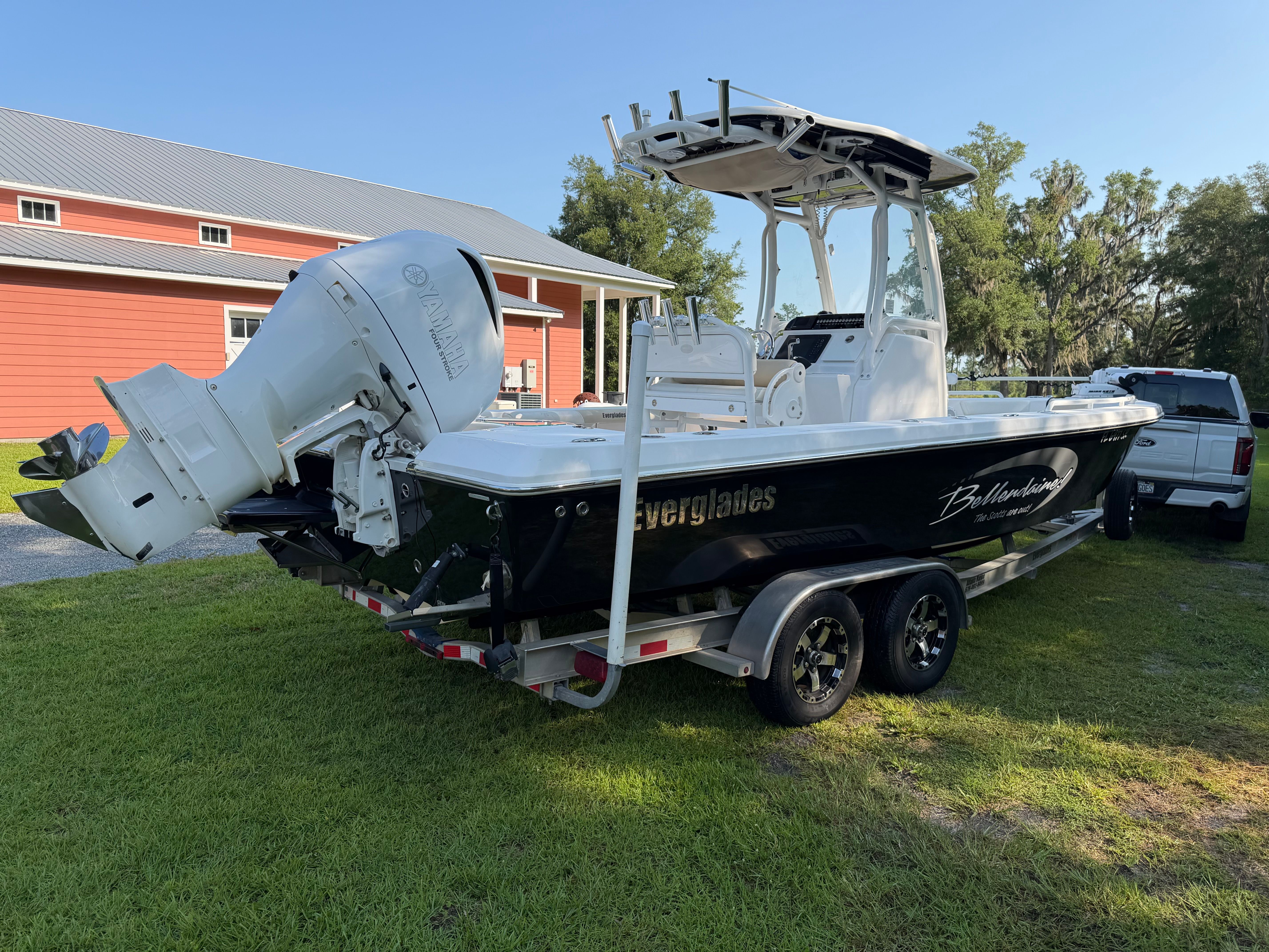 A 2016 Everglades 243 Center Console boat on a trailer beside a red building.
