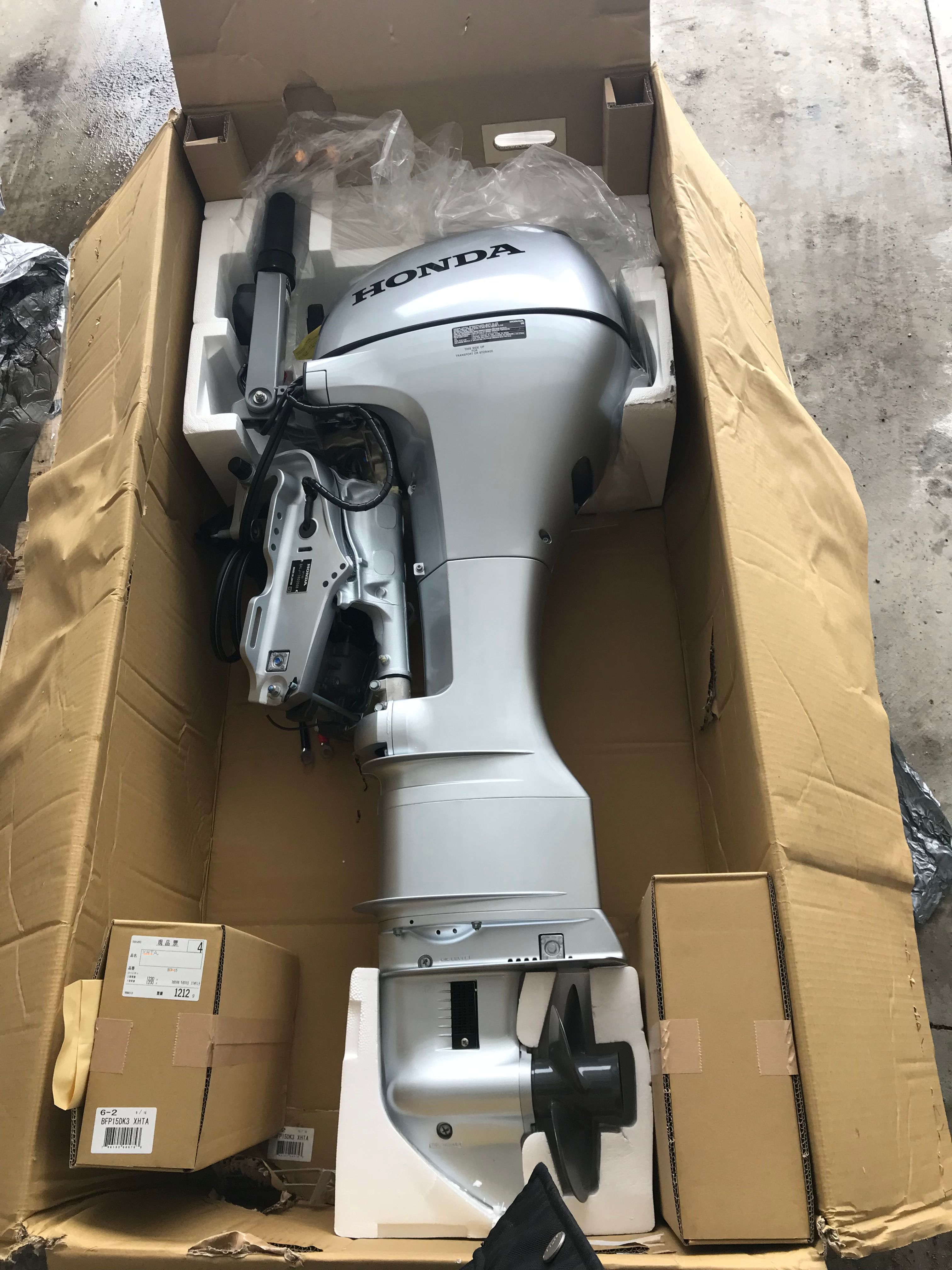 A Honda outboard motor in an open cardboard box on a concrete floor.