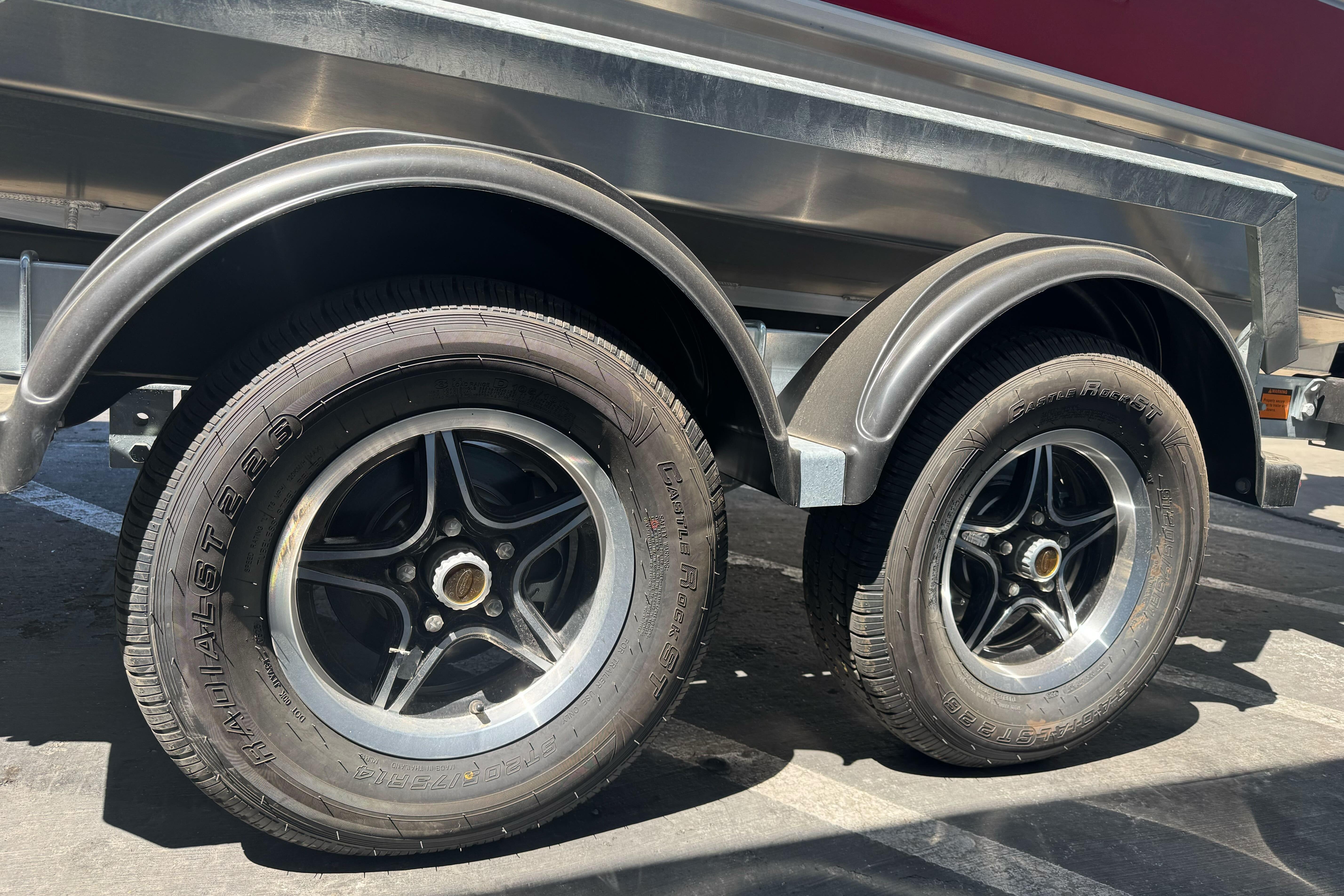 Trailer wheels of a 2026 Lund 210 Heavy Gauge boat, parked on asphalt.