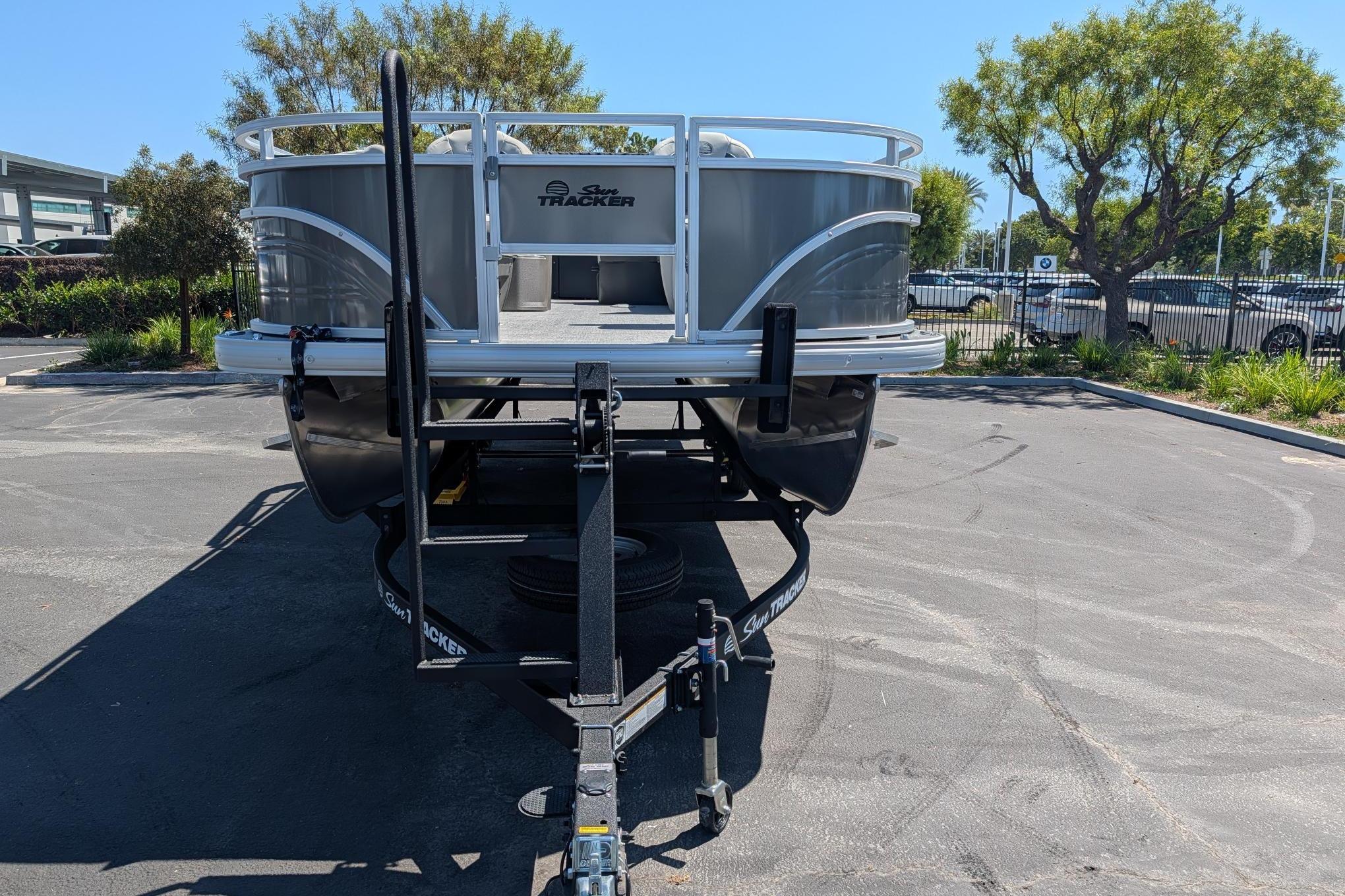 2026 Sun Tracker Fishin' Barge 22 DLX pontoon boat on trailer in parking lot.