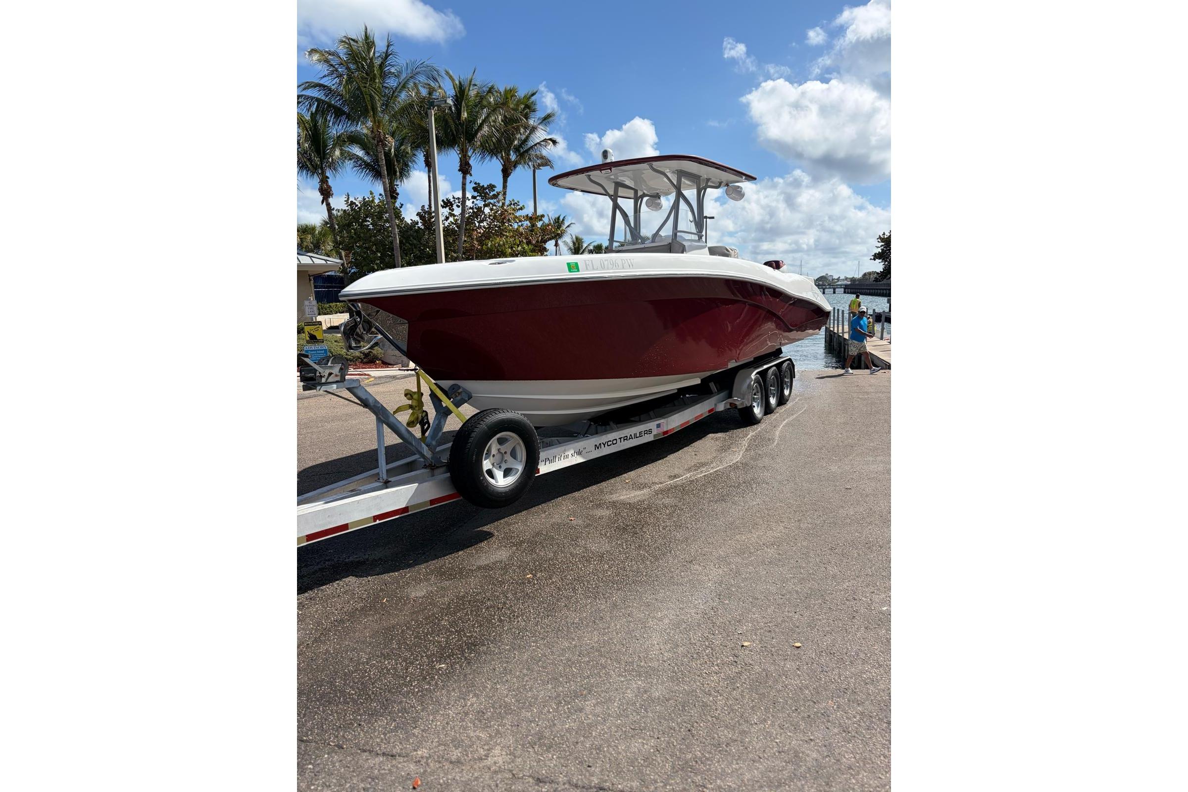 2015 Deep Impact 33 boat on trailer, parked near waterfront with palm trees.