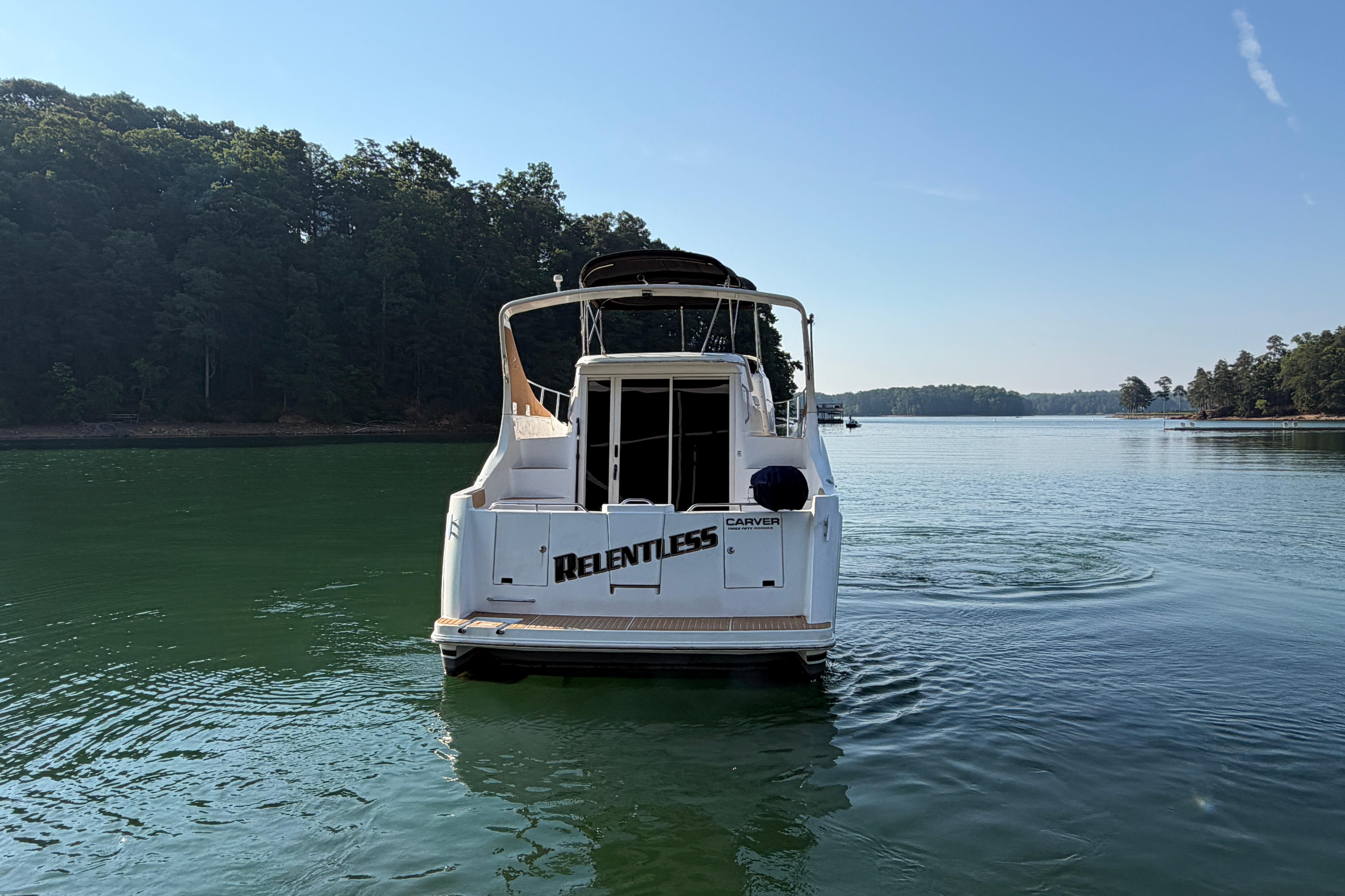 2003 Carver 350 Mariner boat named "Relentless" on a serene lake with forested shoreline.