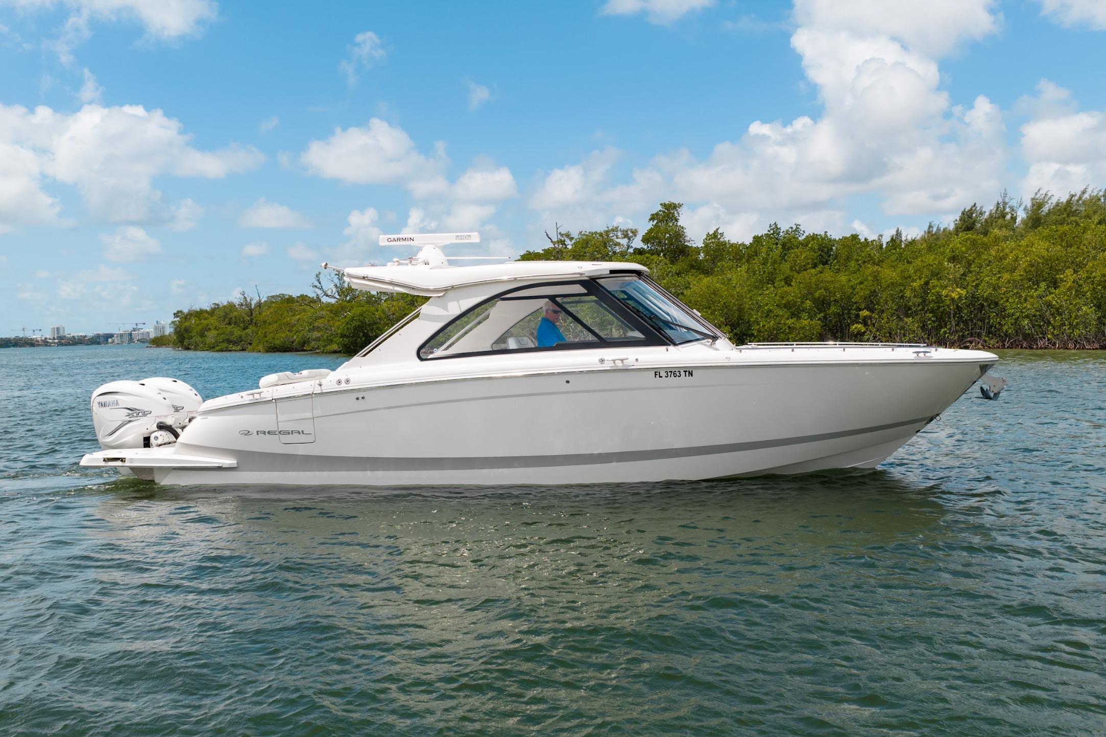 2023 Regal LX36 boat cruising on a sunny day, surrounded by lush greenery.