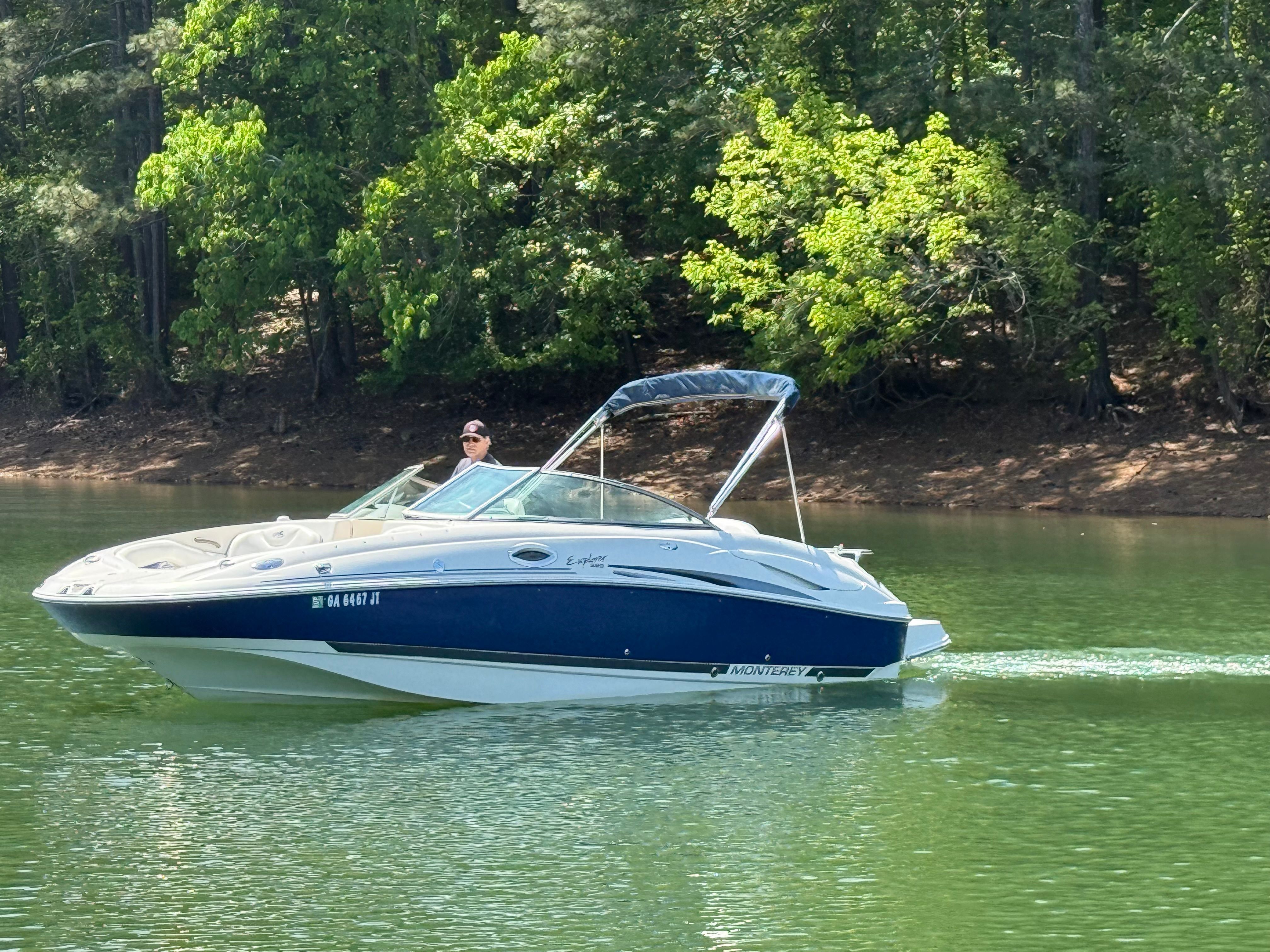 A 2005 Monterey 223 Explorer Sport cruising on a calm lake, surrounded by trees.