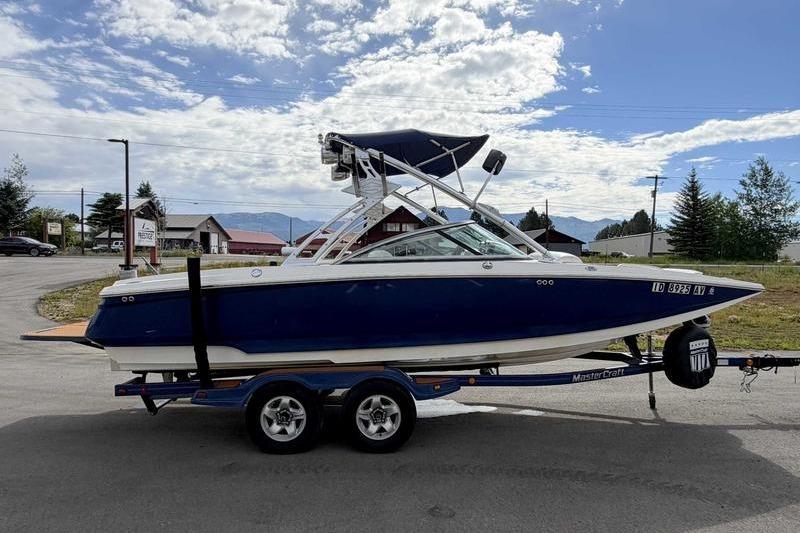 2004 MasterCraft XStar boat on trailer, parked outdoors under a partly cloudy sky.