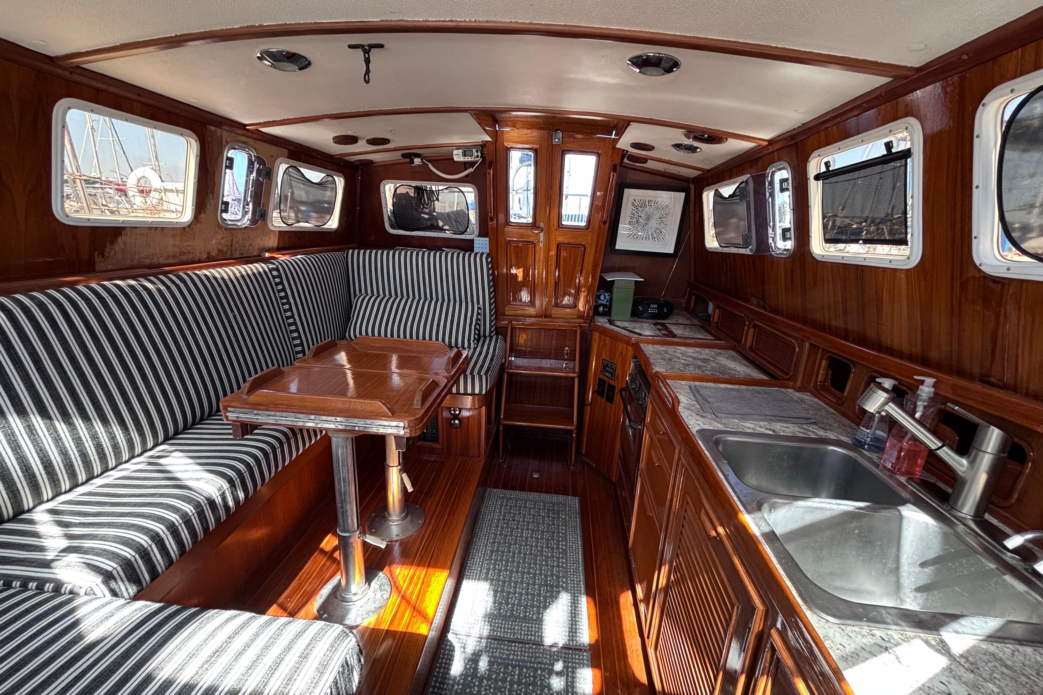 Interior of a 1978 Swift 33 yacht with striped seating, wooden table, and compact kitchen.