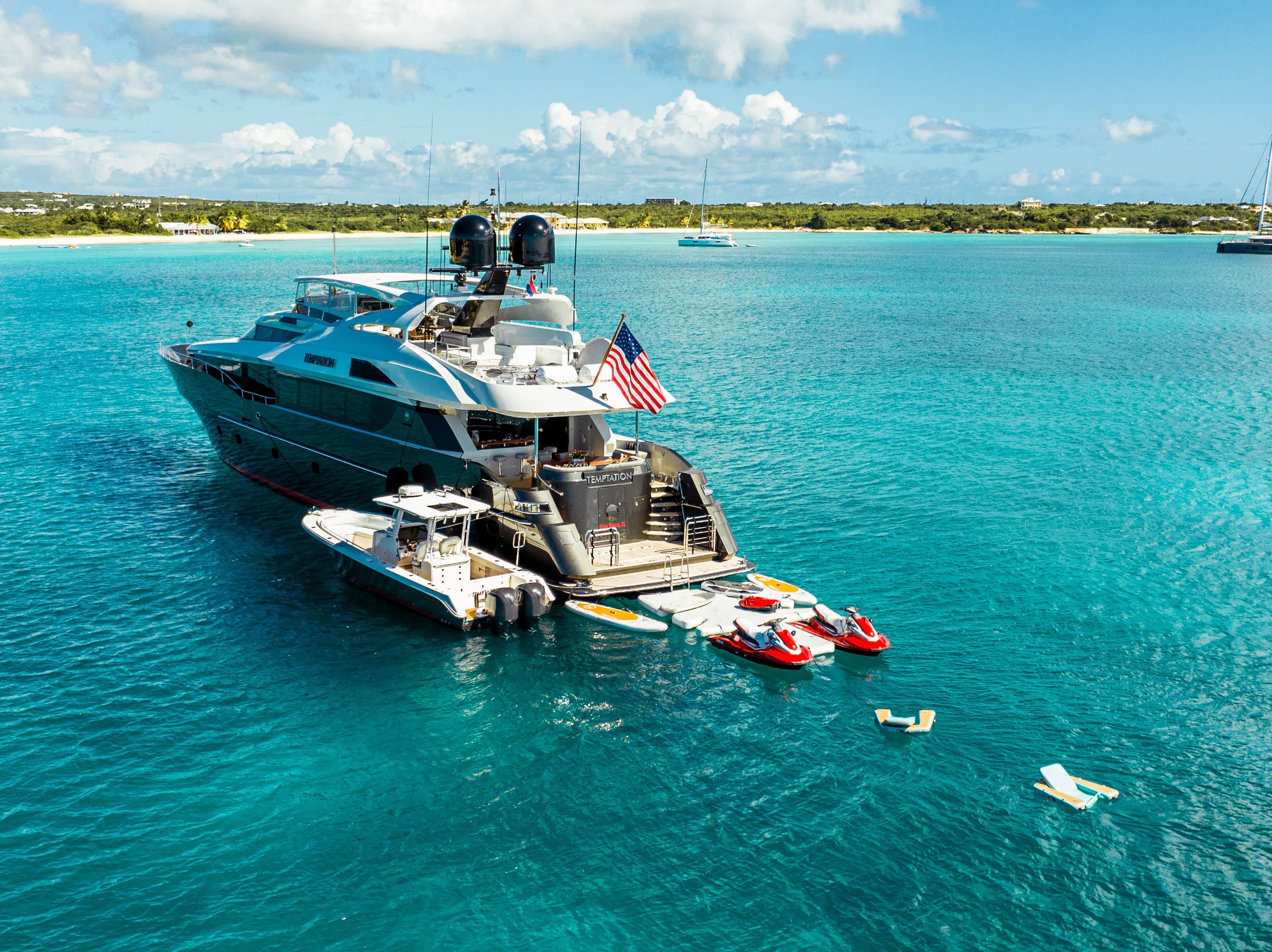 A luxurious 2005 Palmer Johnson yacht anchored in clear blue water, with water toys nearby.
