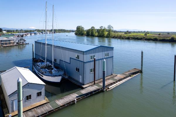 A 1985 Custom Larson Boathouse with sailboat on a serene river.