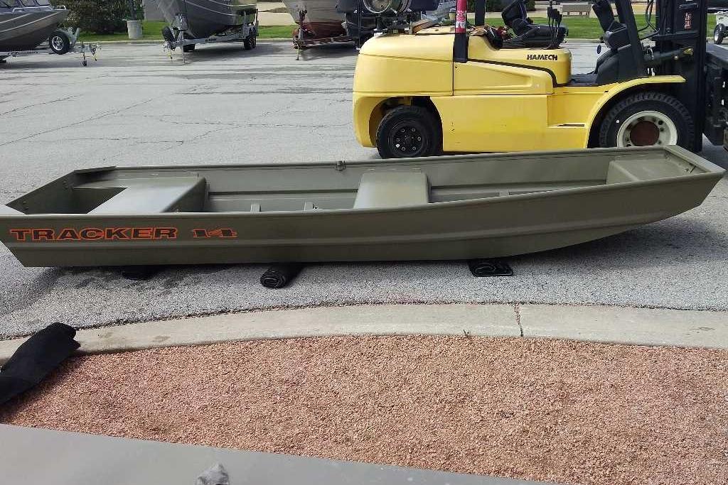 2026 Tracker Grizzly 14 Jon boat on pavement near a yellow forklift.