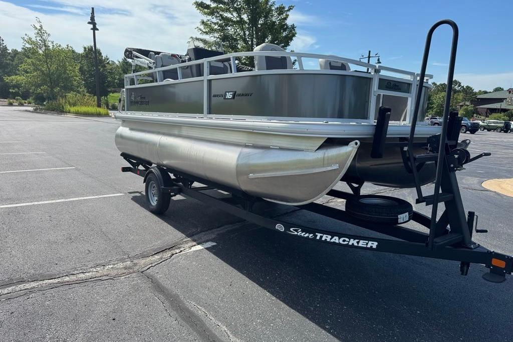 2026 Sun Tracker Bass Buggy 16 XL Select pontoon boat on trailer in parking lot.