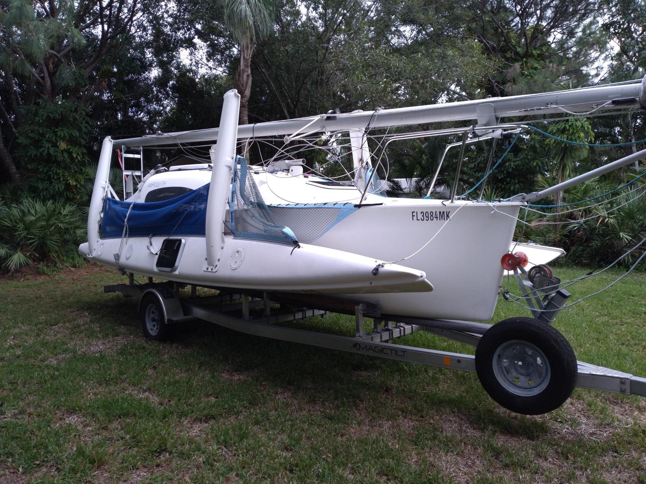 2004 Corsair F-24MKII sailboat on trailer, parked on grass, surrounded by trees.