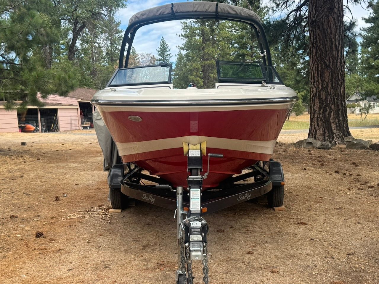 A red 2016 Sea Ray SPX 190 Outboard boat on a trailer in a wooded area.