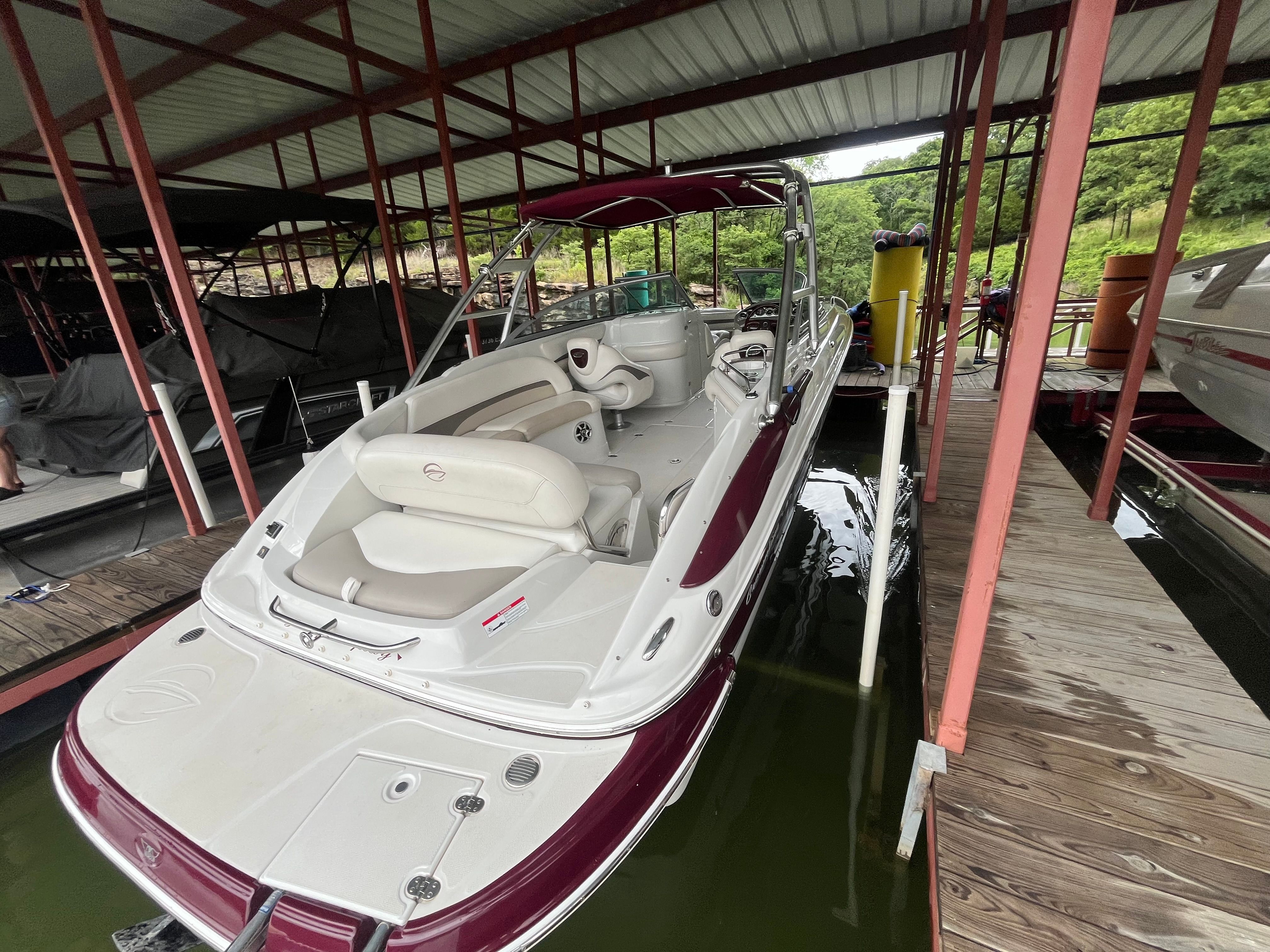 A 2008 Crownline 252EX boat is docked under a covered area. It features white and burgundy upholstery.