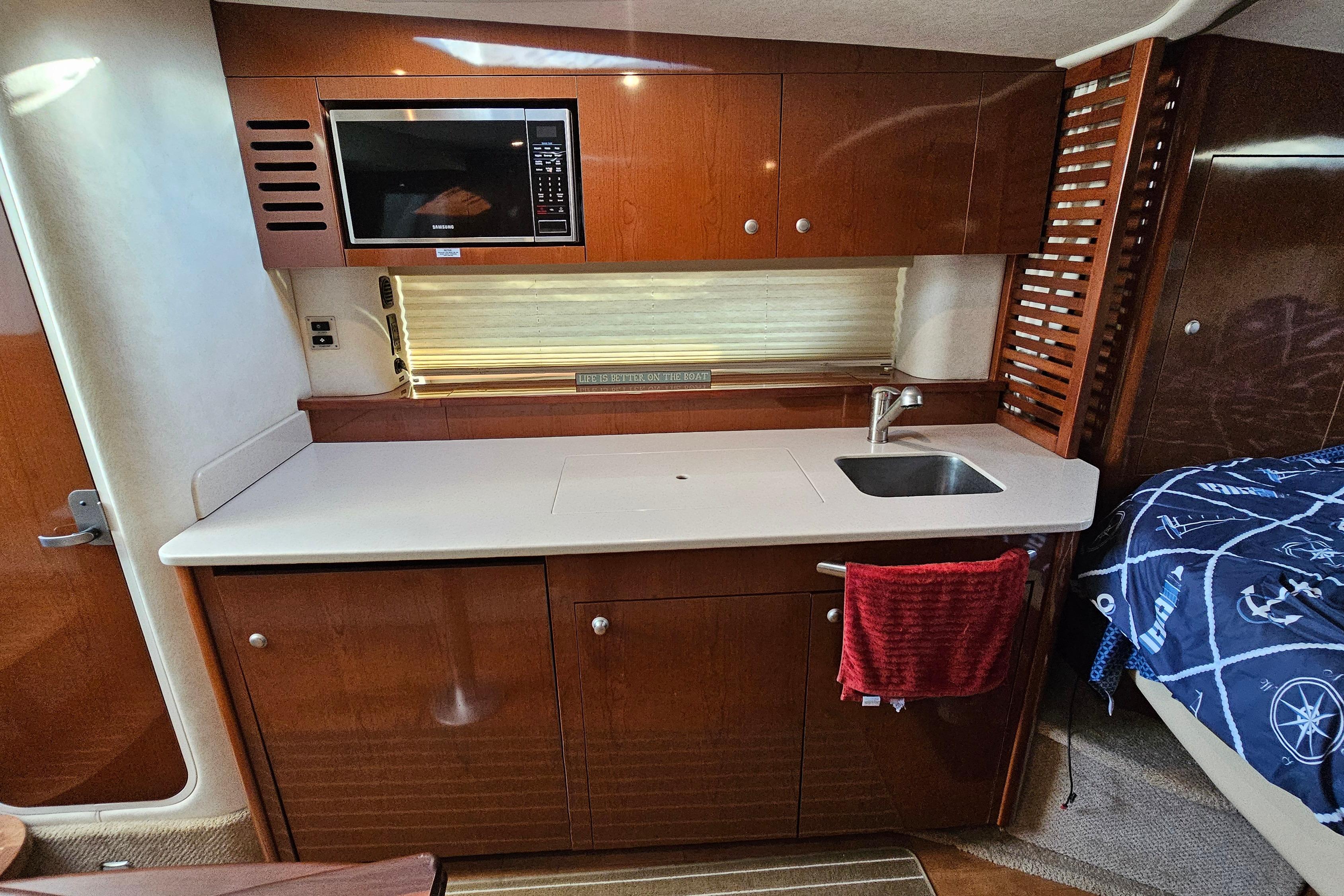 2008 Sea Ray Sundancer 350 interior kitchen with microwave, sink, and wooden cabinetry.