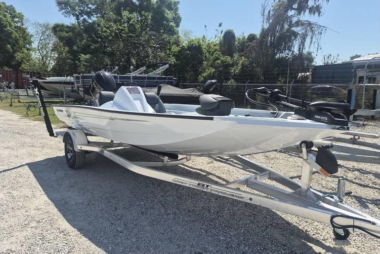 2026 Xpress H18 boat on trailer, parked outdoors, surrounded by trees and other boats.