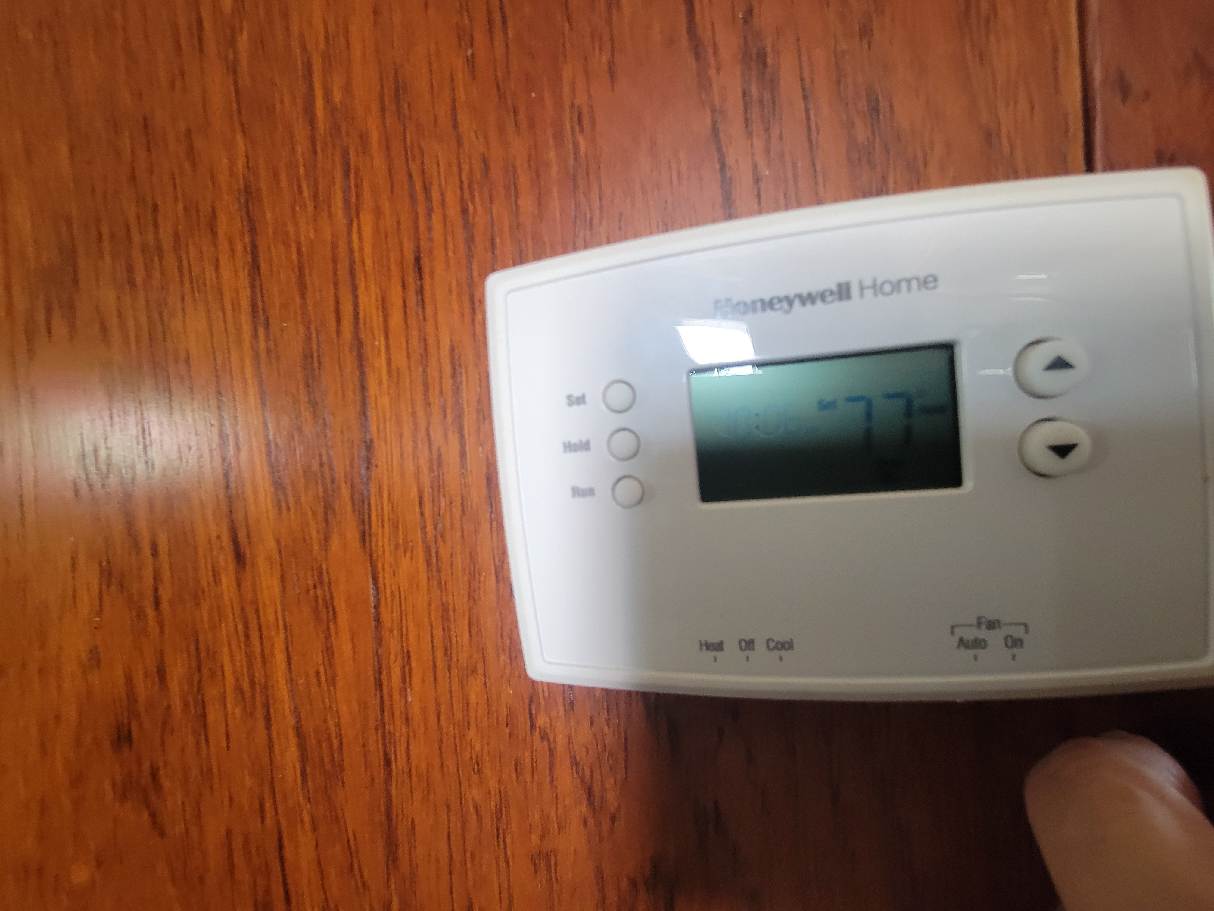A thermostat on a wooden wall displays 77 degrees Fahrenheit.