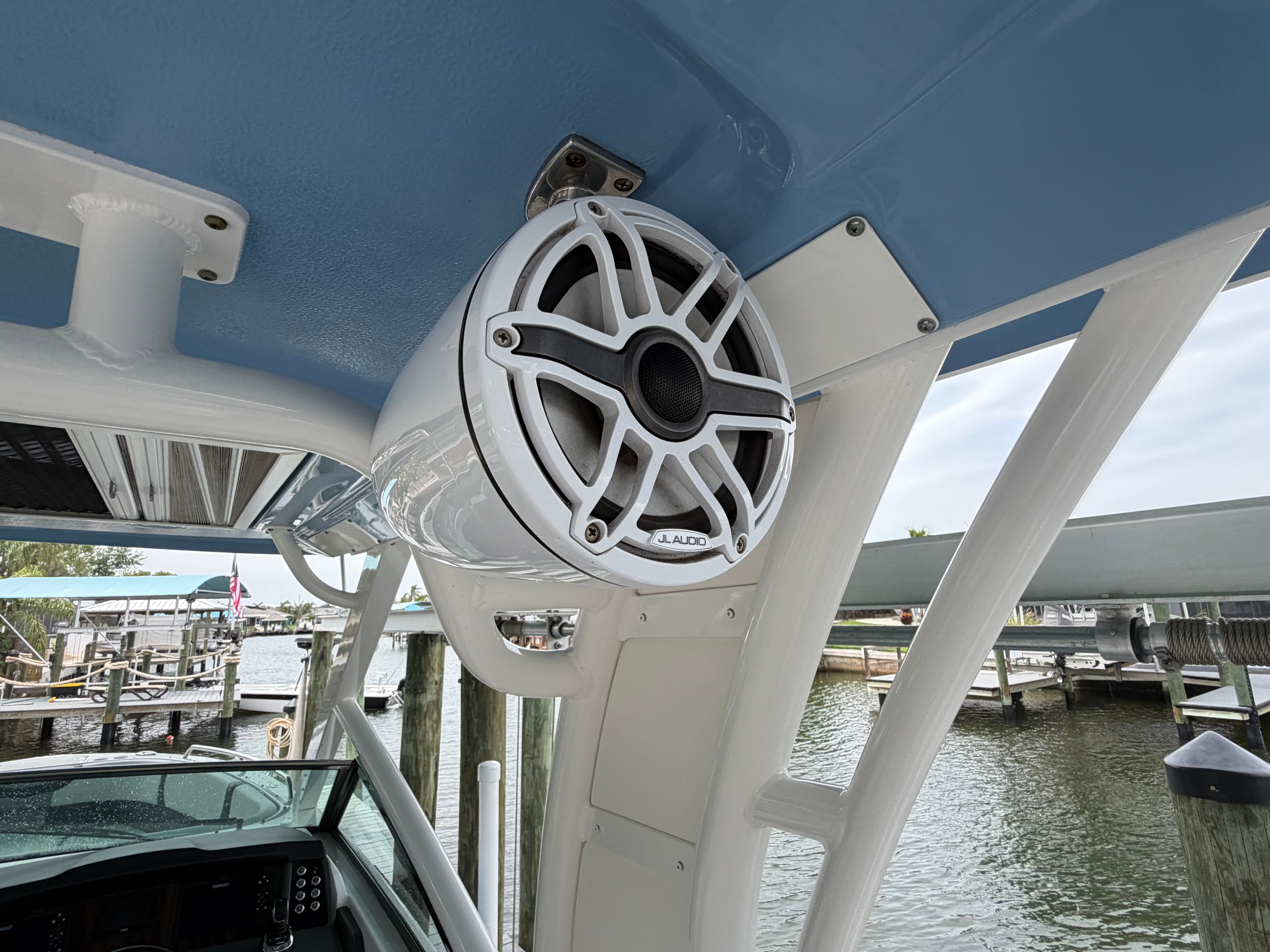 A speaker is mounted on the blue ceiling of a boat, with water in the background.