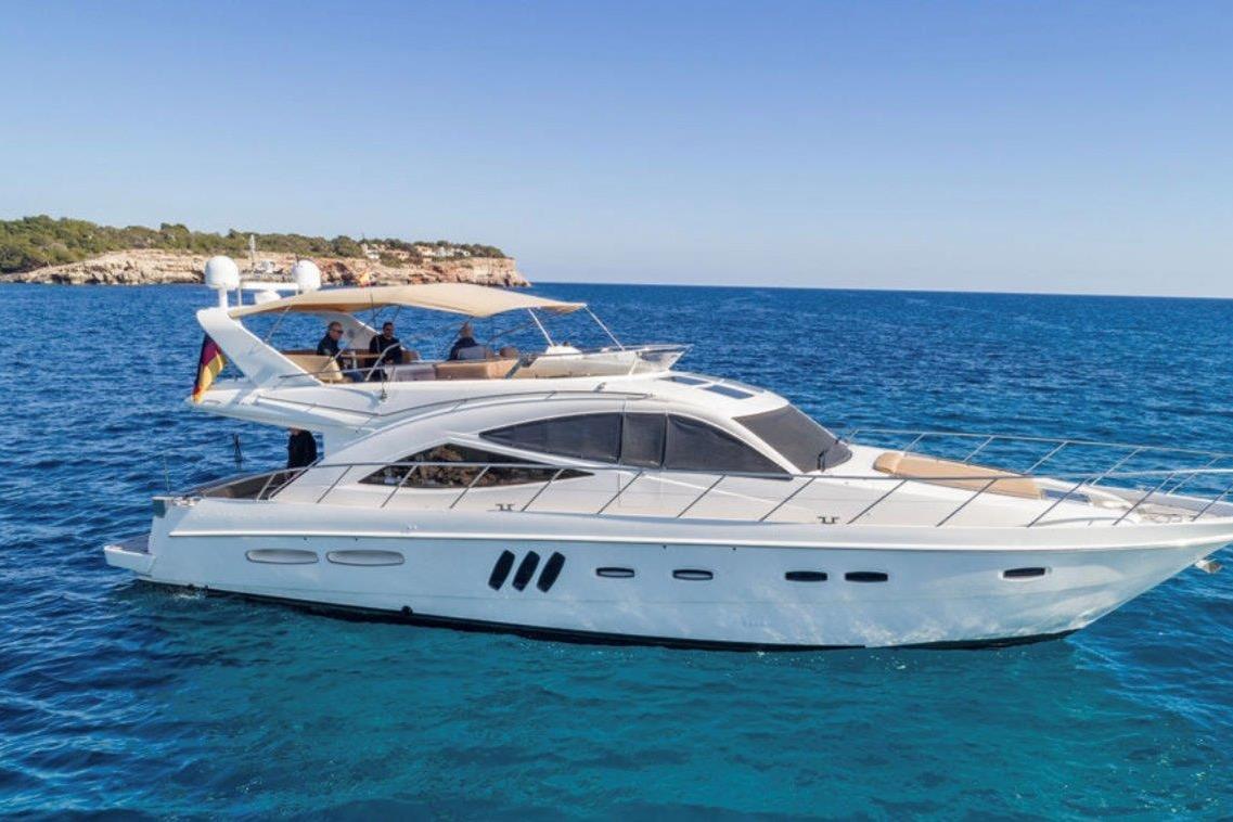 2009 Sealine T60 yacht cruising on clear blue waters near a rocky coastline.