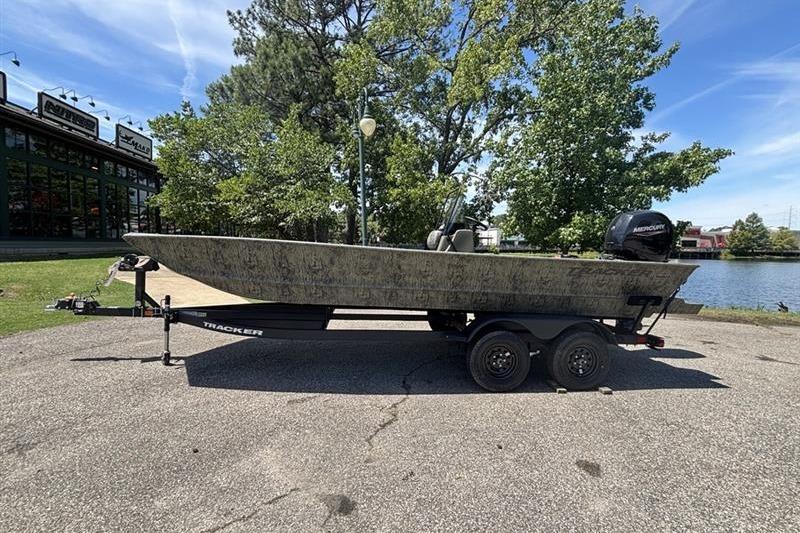 2026 Tracker Grizzly 2072 CC boat on trailer, parked near a lake with trees in the background.