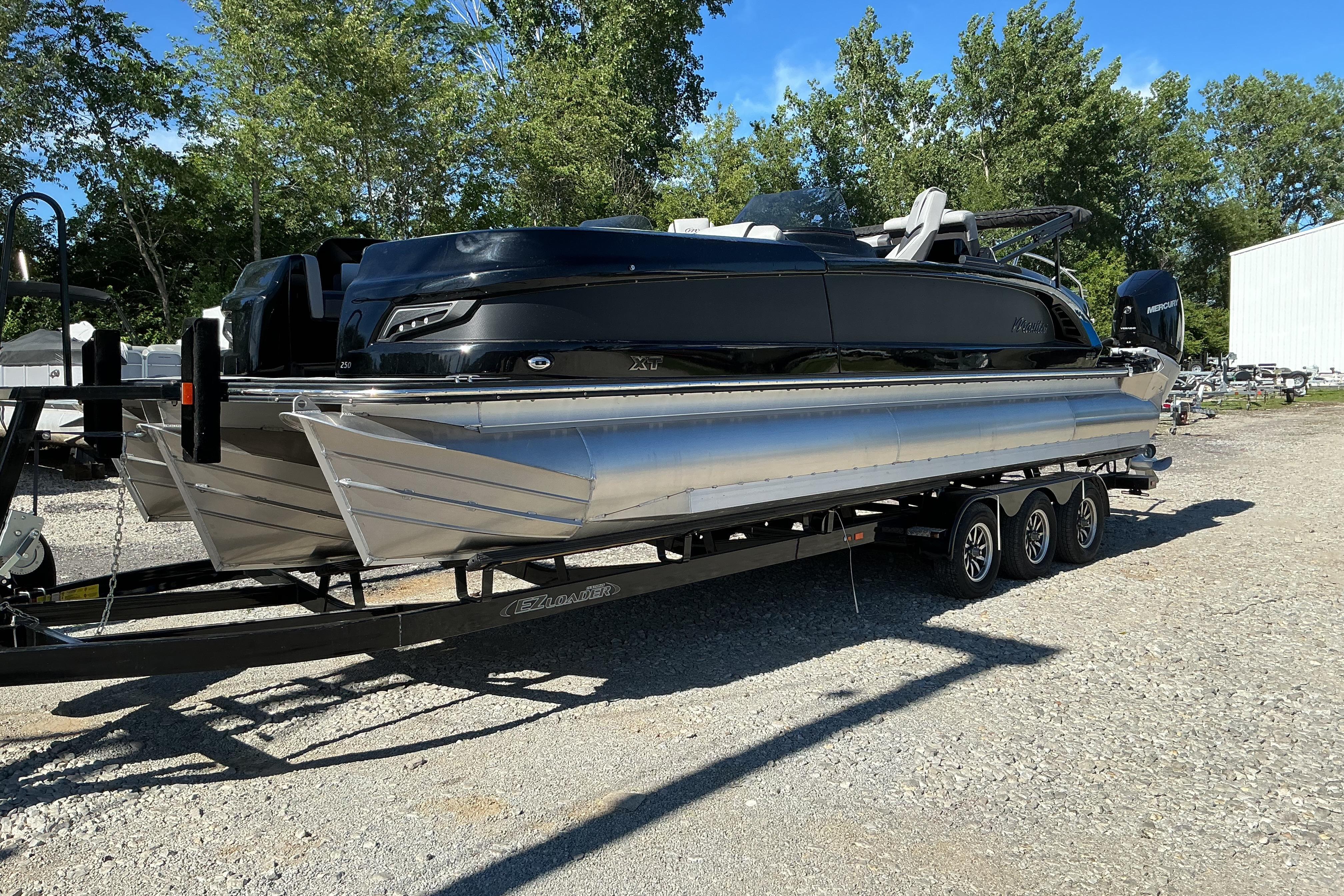 2024 Manitou 25 X-Plode XT SRS pontoon boat on trailer, parked outdoors.