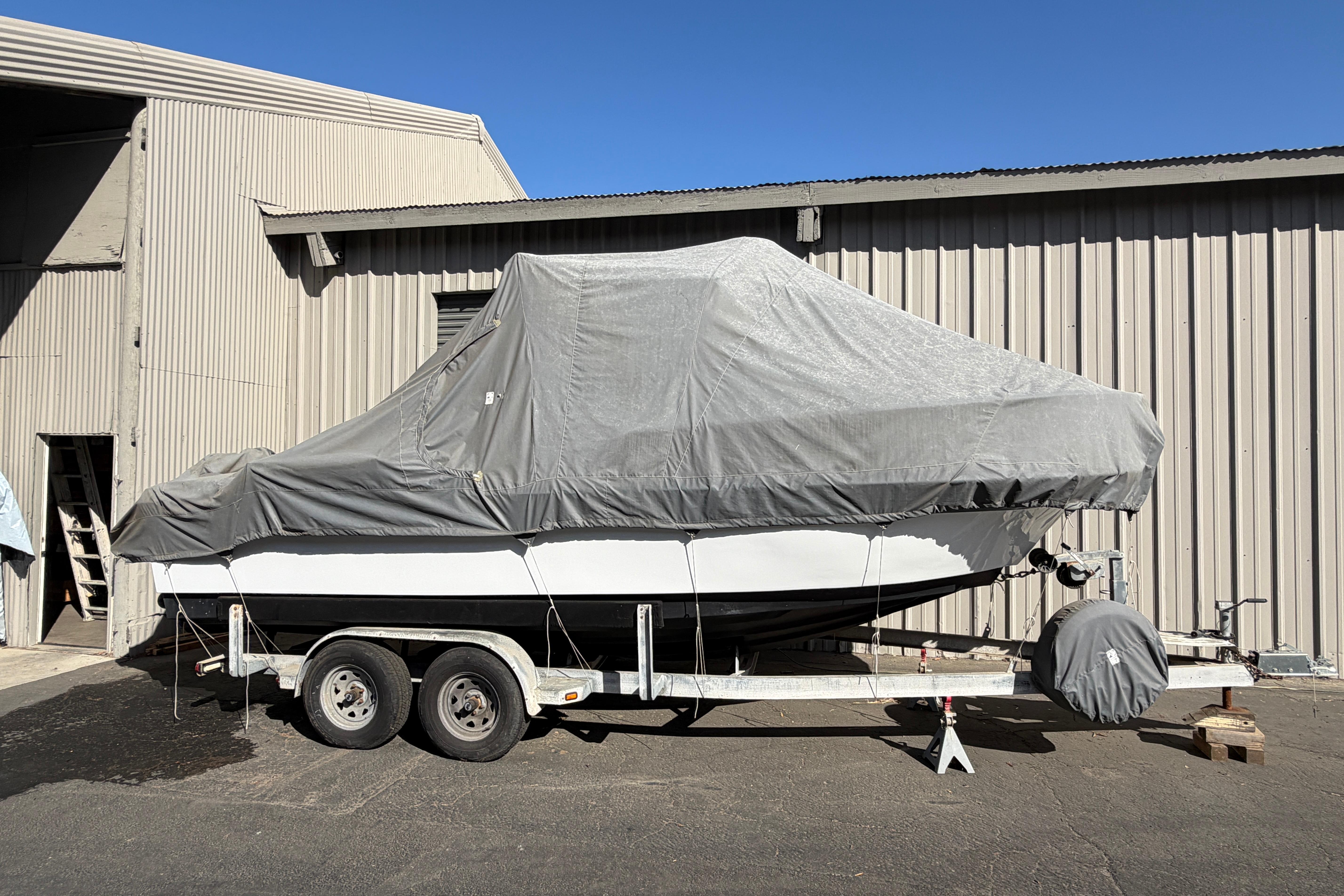 Covered 1986 Radon 21 Sport boat on trailer beside industrial building.