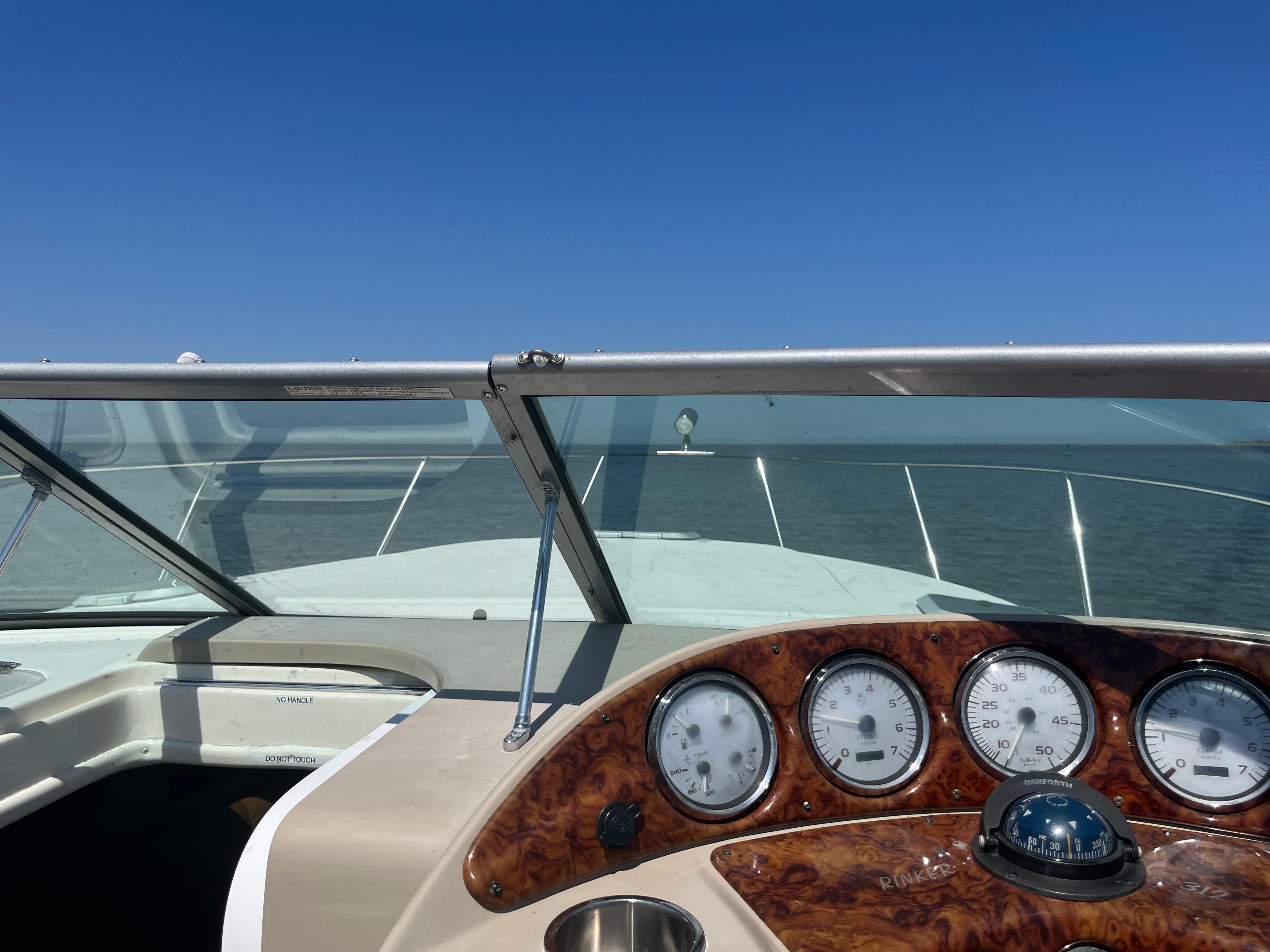 2003 Rinker Fiesta Vee 312 boat dashboard with gauges, cruising on open water under clear blue sky.