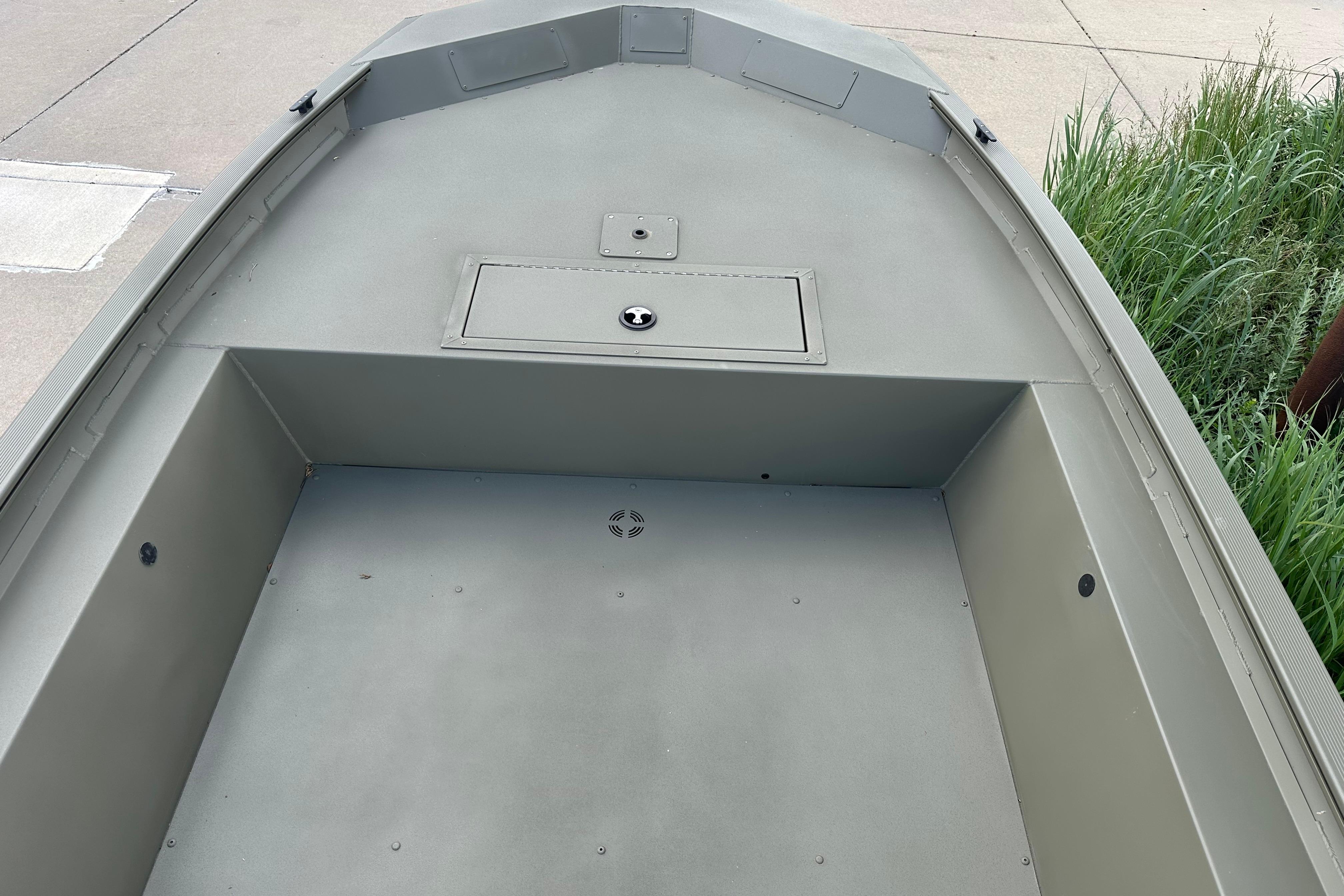 2026 Tracker Grizzly 1754 Utility boat interior with storage compartment, docked near greenery.