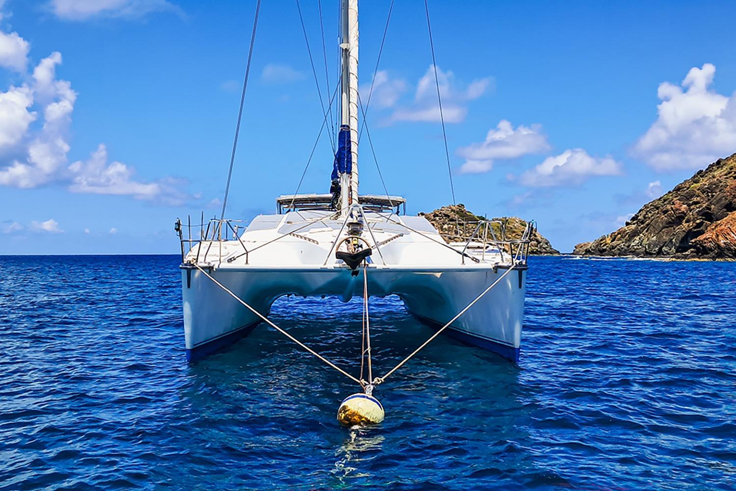 Catamaran Privilege 39, 1992 model, anchored in clear blue waters with rocky islands.