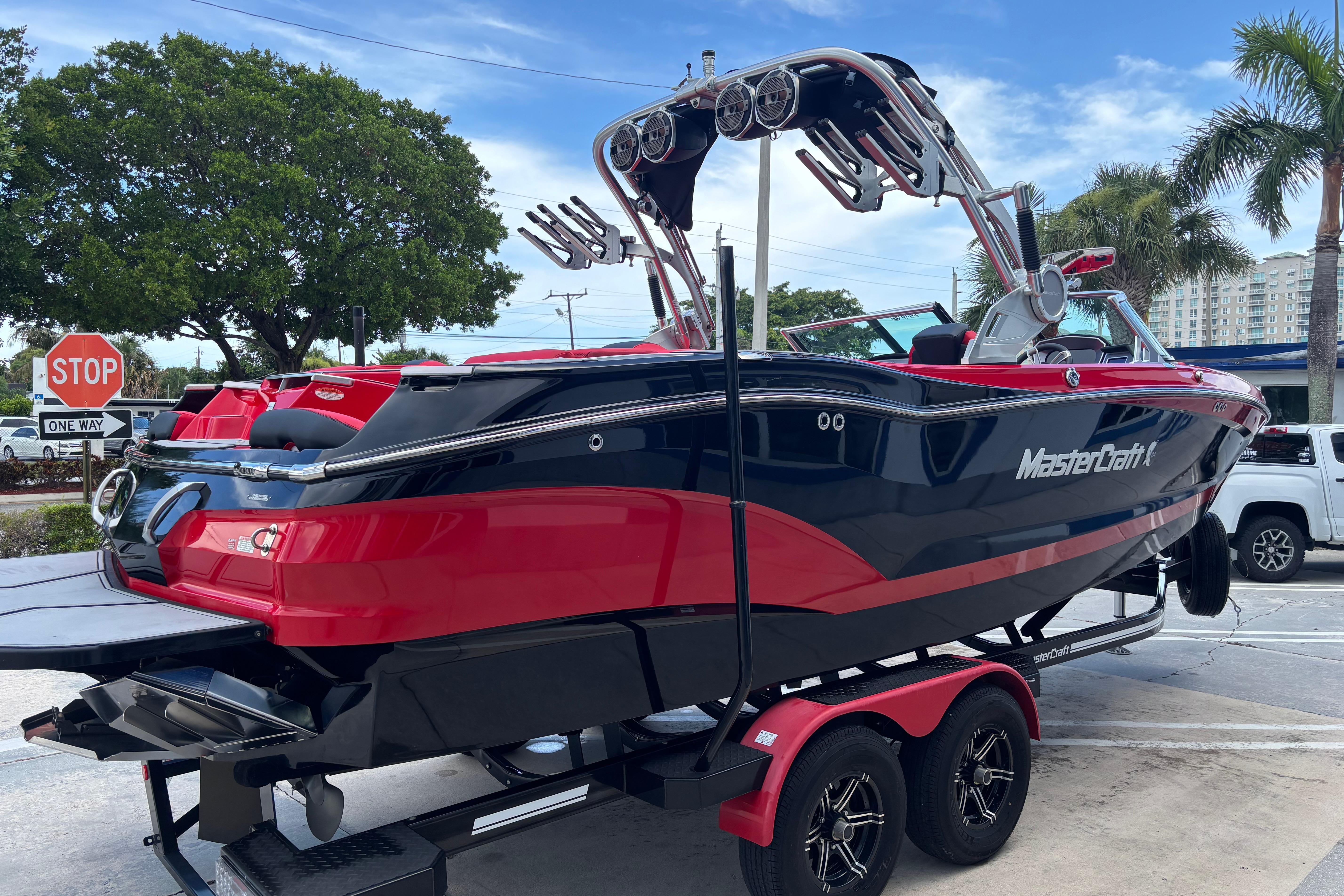 2020 MasterCraft X24 boat on trailer, red and black design, parked near palm trees.