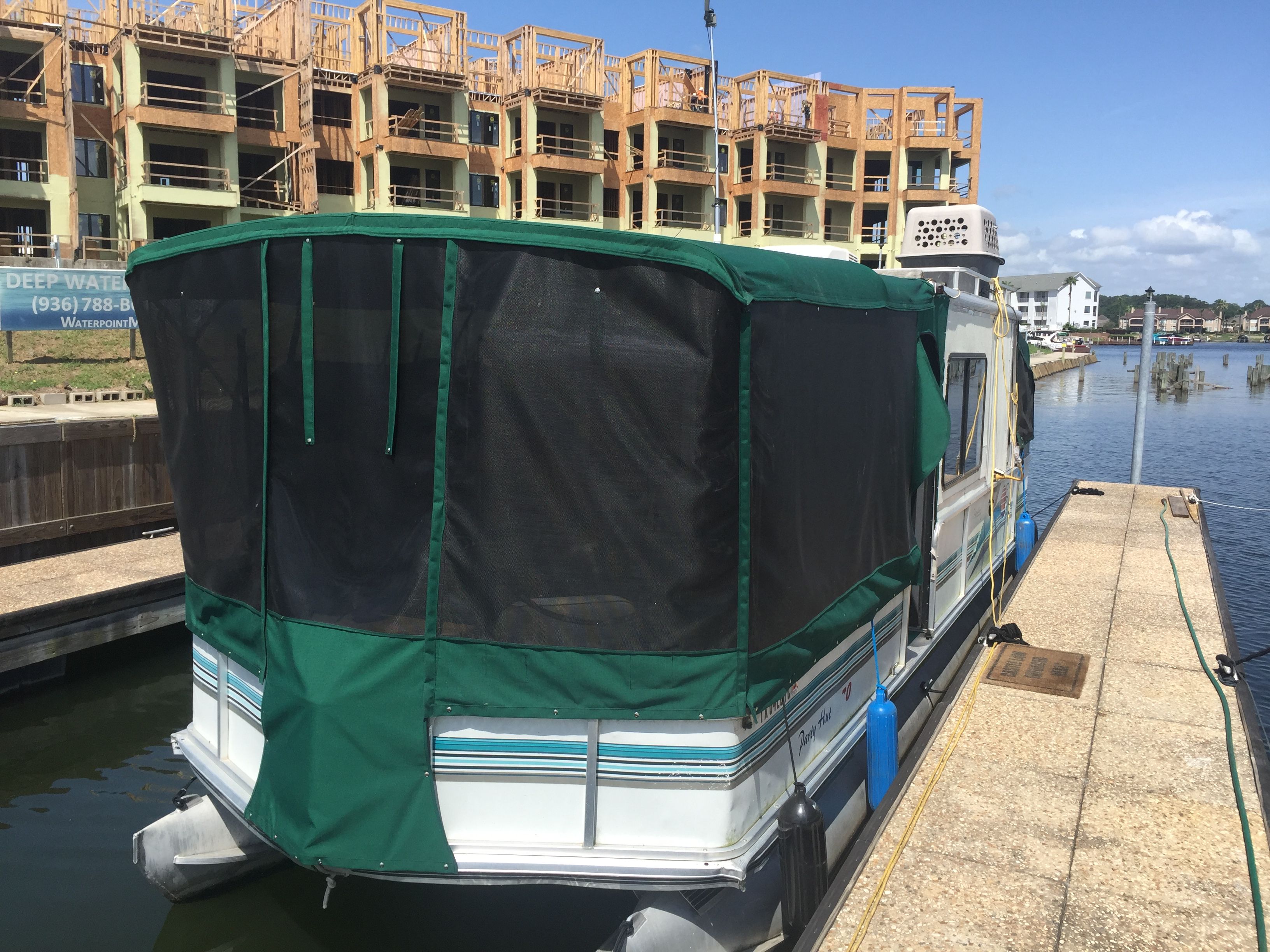 A boat with a green canopy docked beside a pier, with a building under construction nearby.