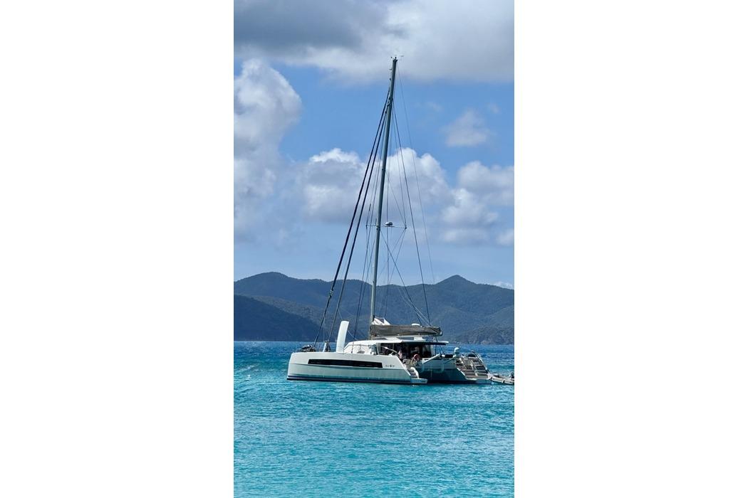 2021 Catana 53 catamaran sailing in turquoise waters with mountainous backdrop.