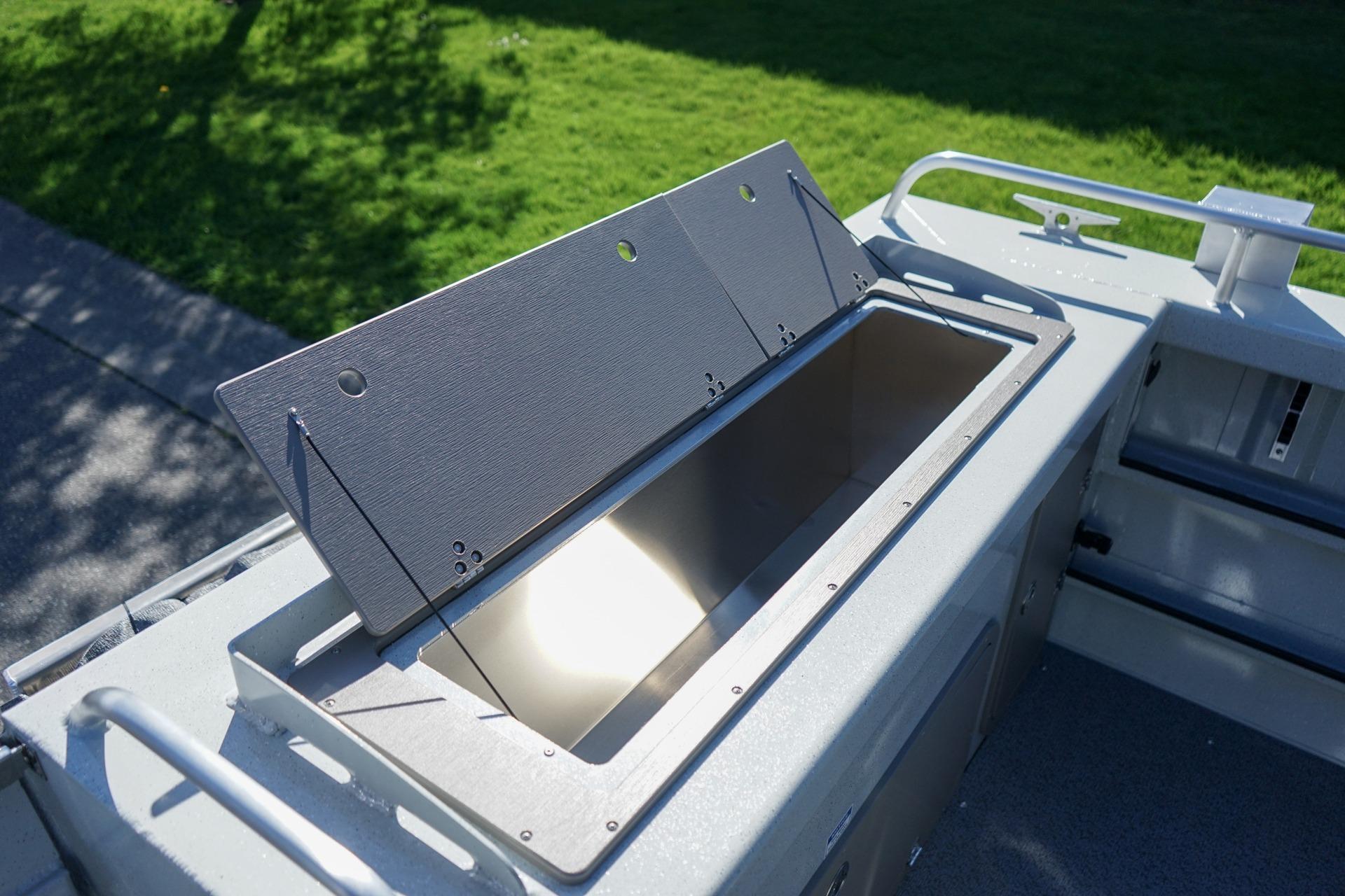 Open storage compartment on 2026 Weldcraft 210 Revolution boat, with green grass background.