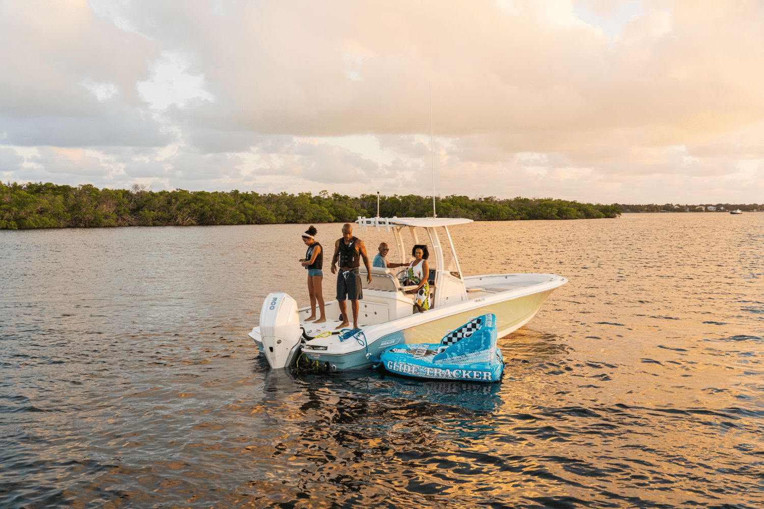 Three people stand on a Boston Whaler 25DA boat on calm water at sunset.