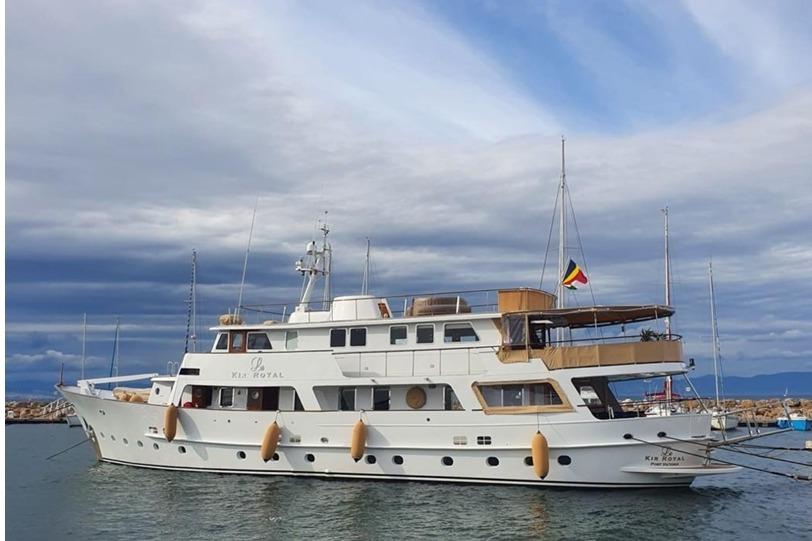 1966 Full Displacement Motor Yacht in harbor, under cloudy sky, side view.