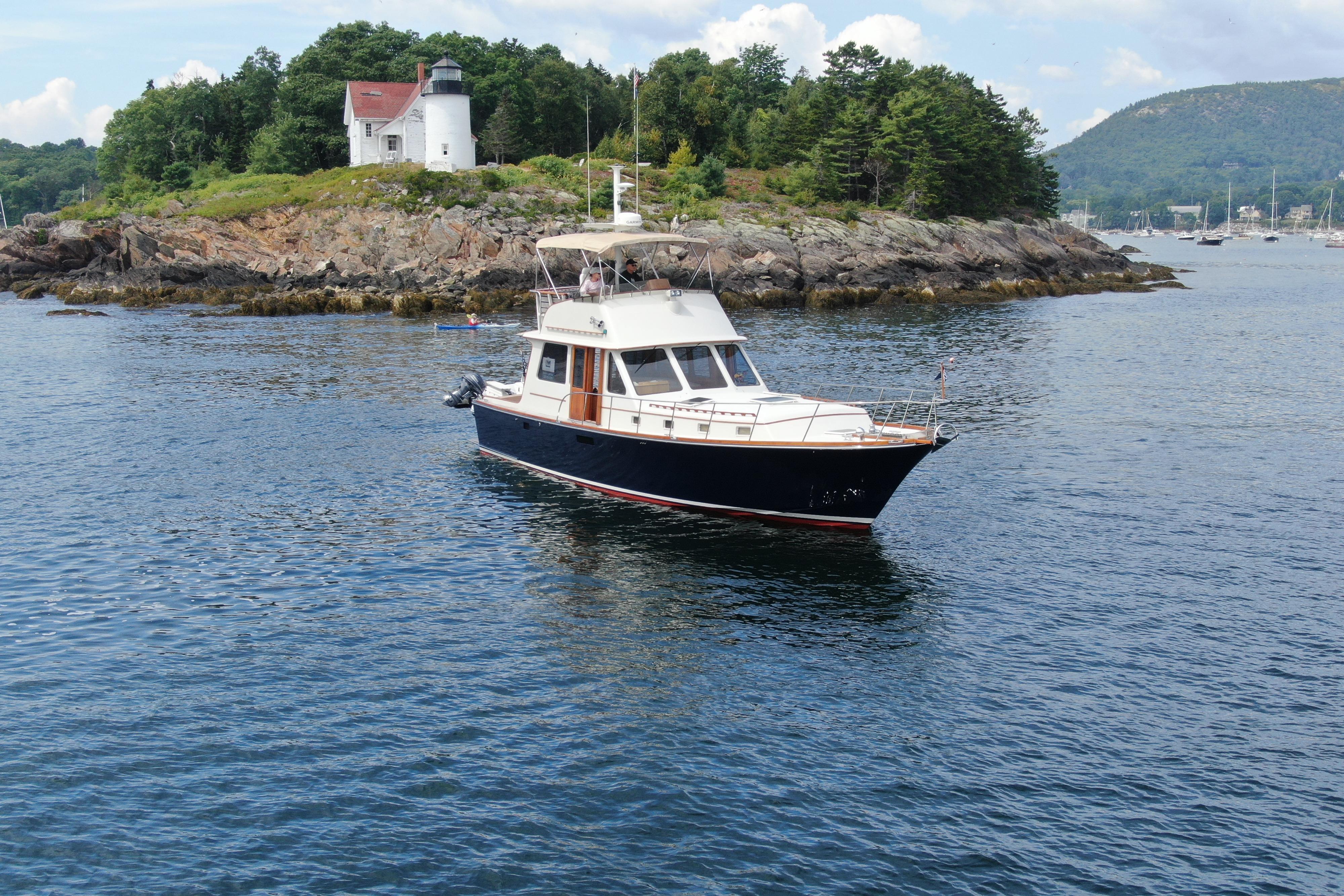 1997 Lyman-Morse Custom Flybridge yacht near rocky shoreline with lighthouse in background.