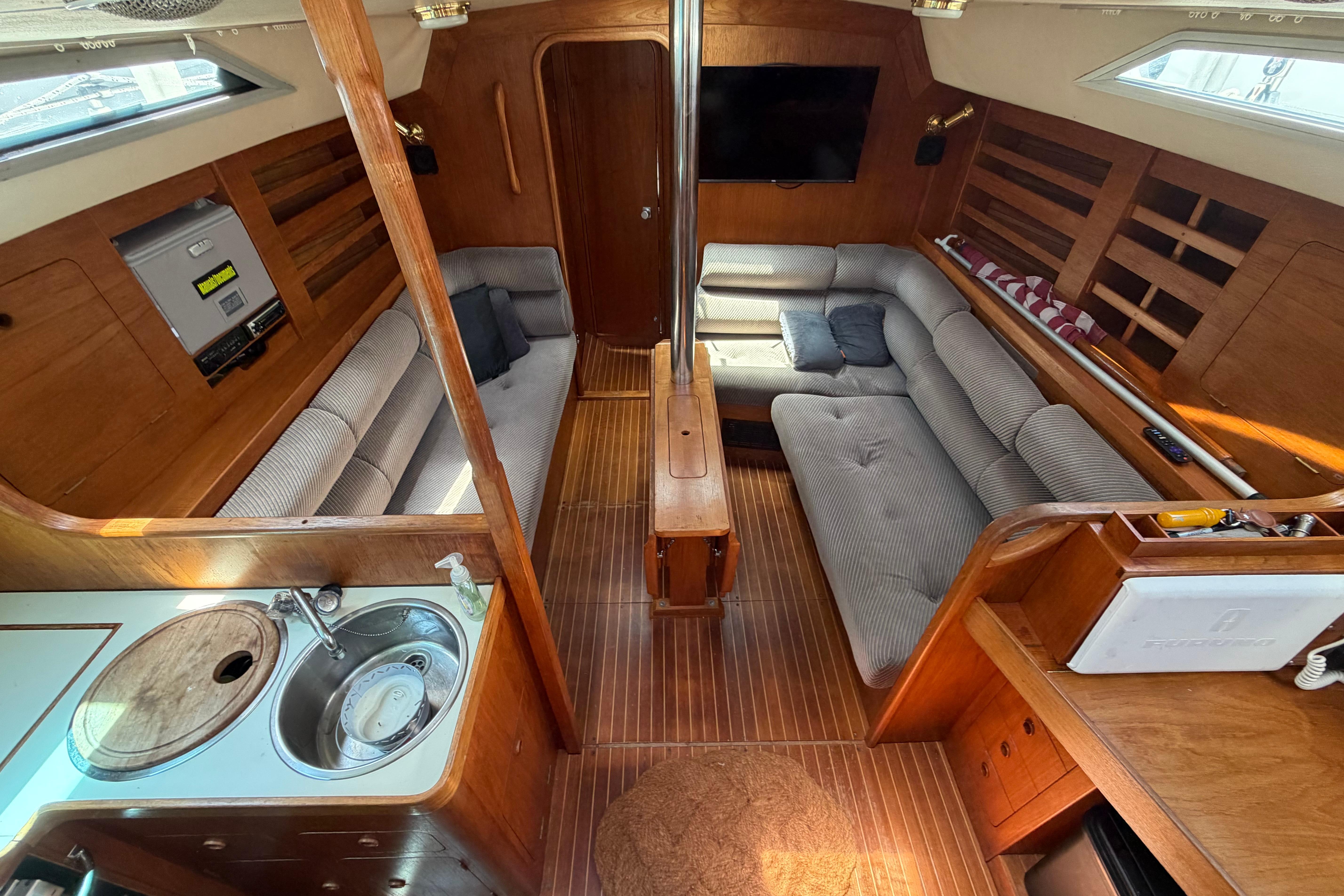 Cozy 1987 Moody 376 yacht interior with wooden finish, plush seating, and compact kitchen area.
