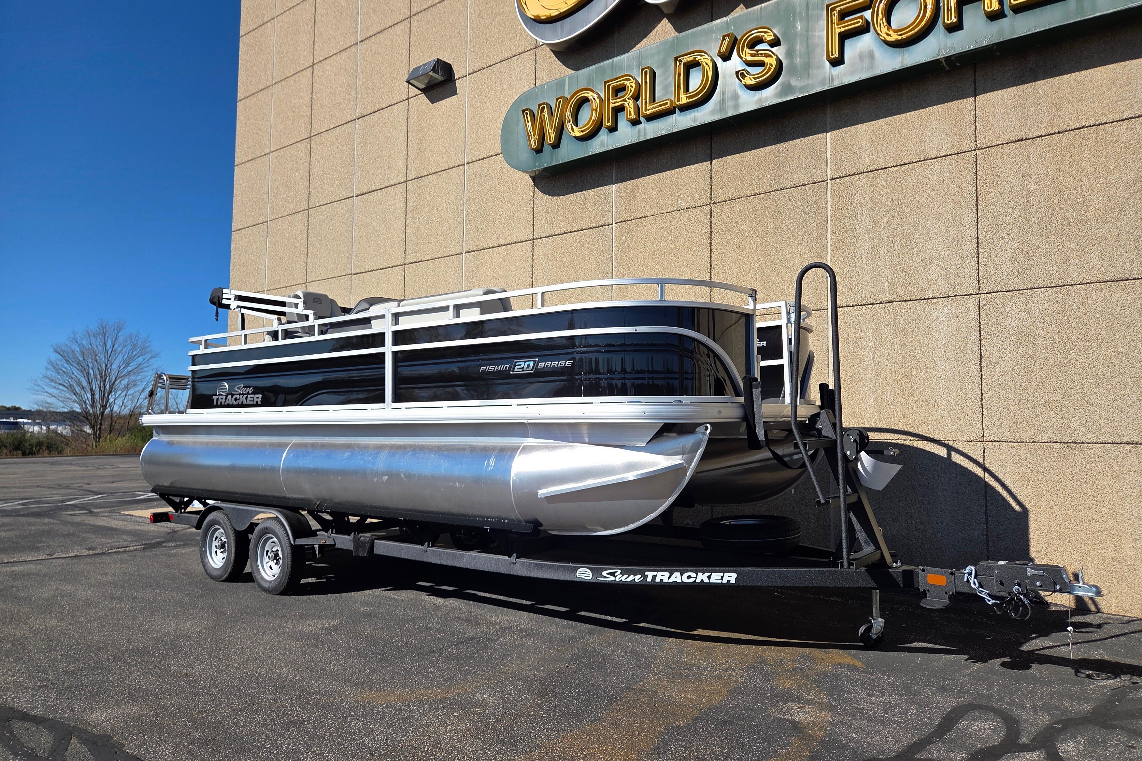 2026 Sun Tracker Fishin' Barge 20 DLX pontoon boat on trailer, parked outdoors.
